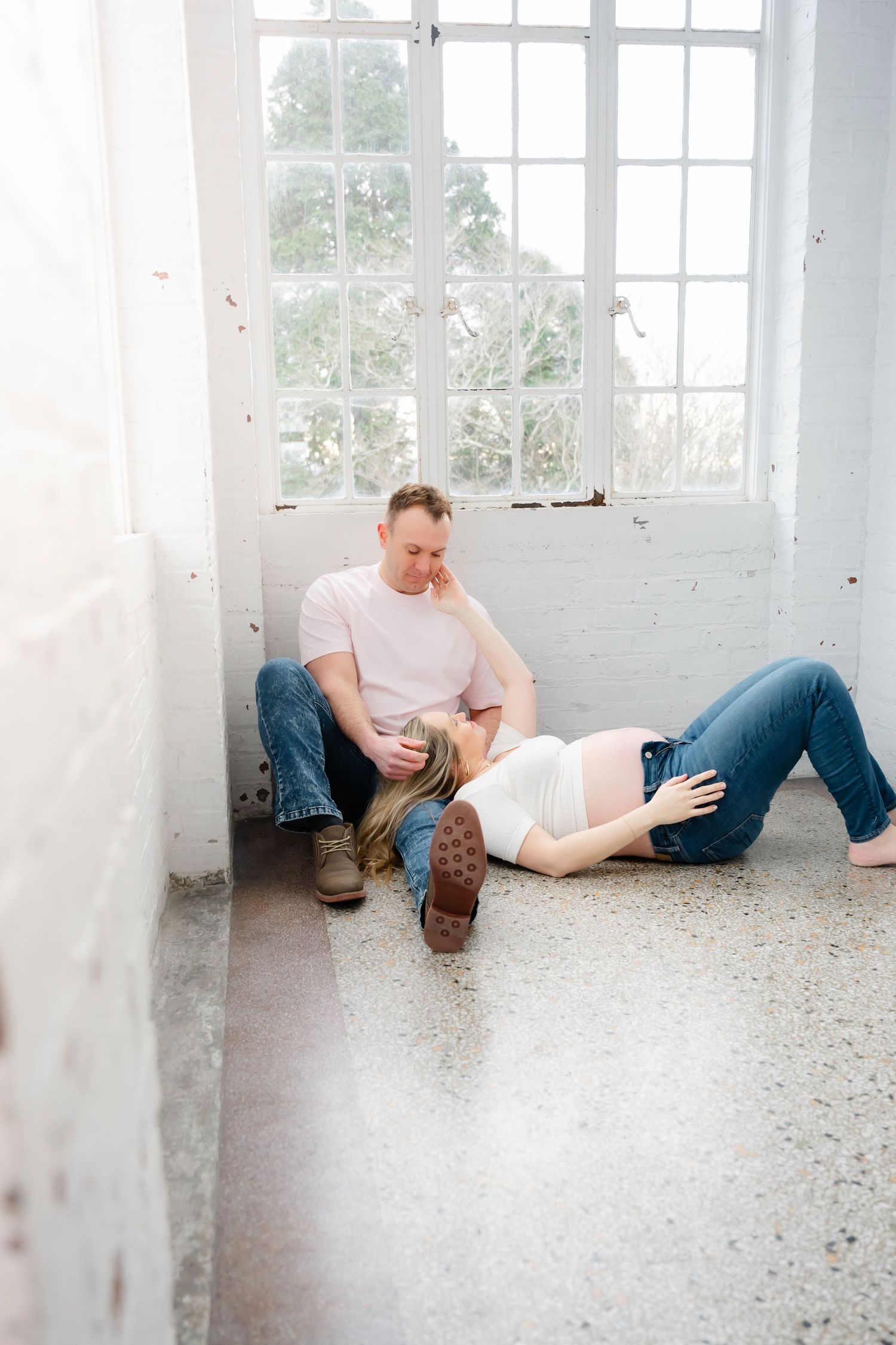 A couple relaxes on the floor of a bright white room with large windows.