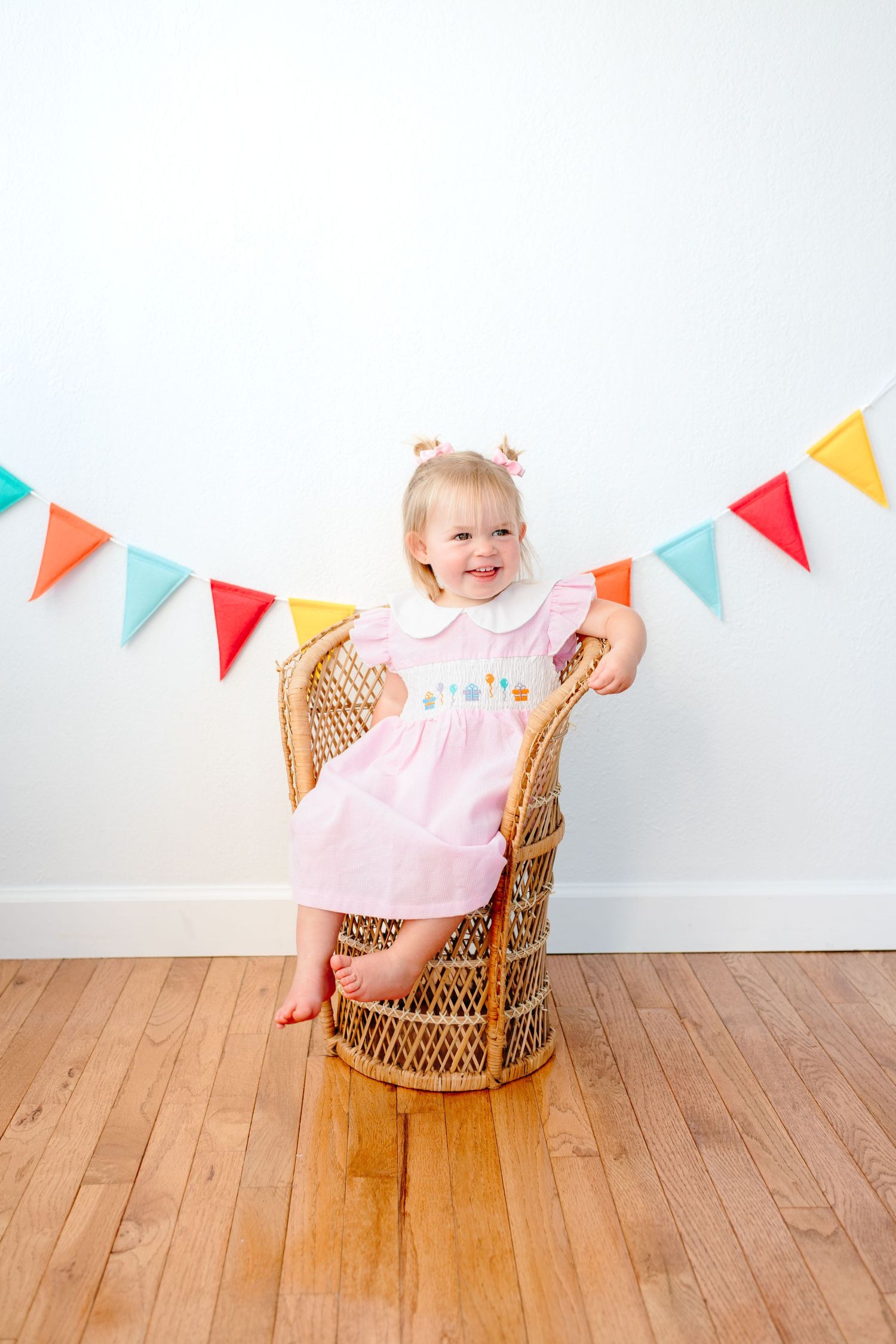 Colorful bunting decorates wall behind wicker chair in birthday photo setup.