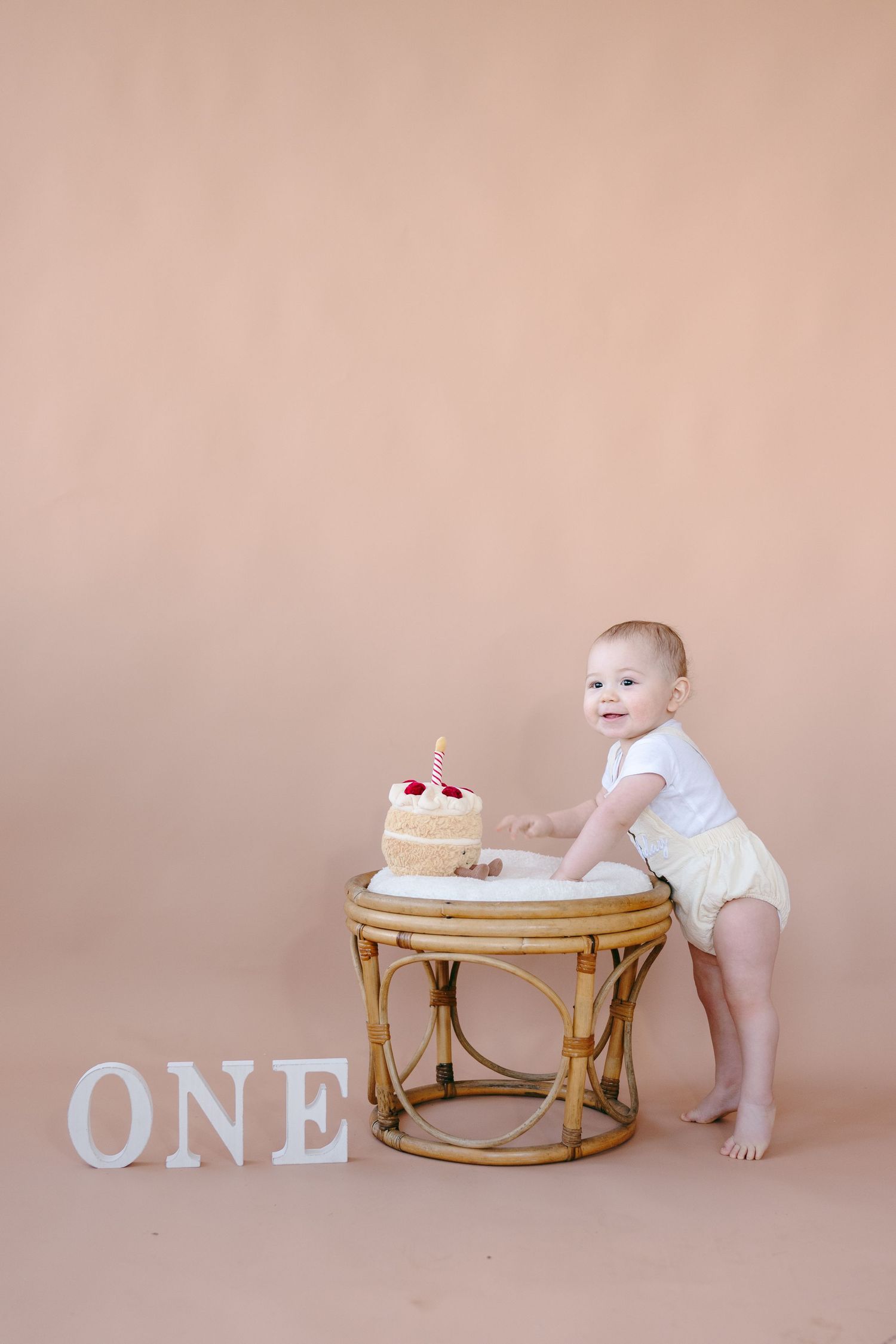 Baby explores round rattan table with 'ONE' letters and decorative elements.
