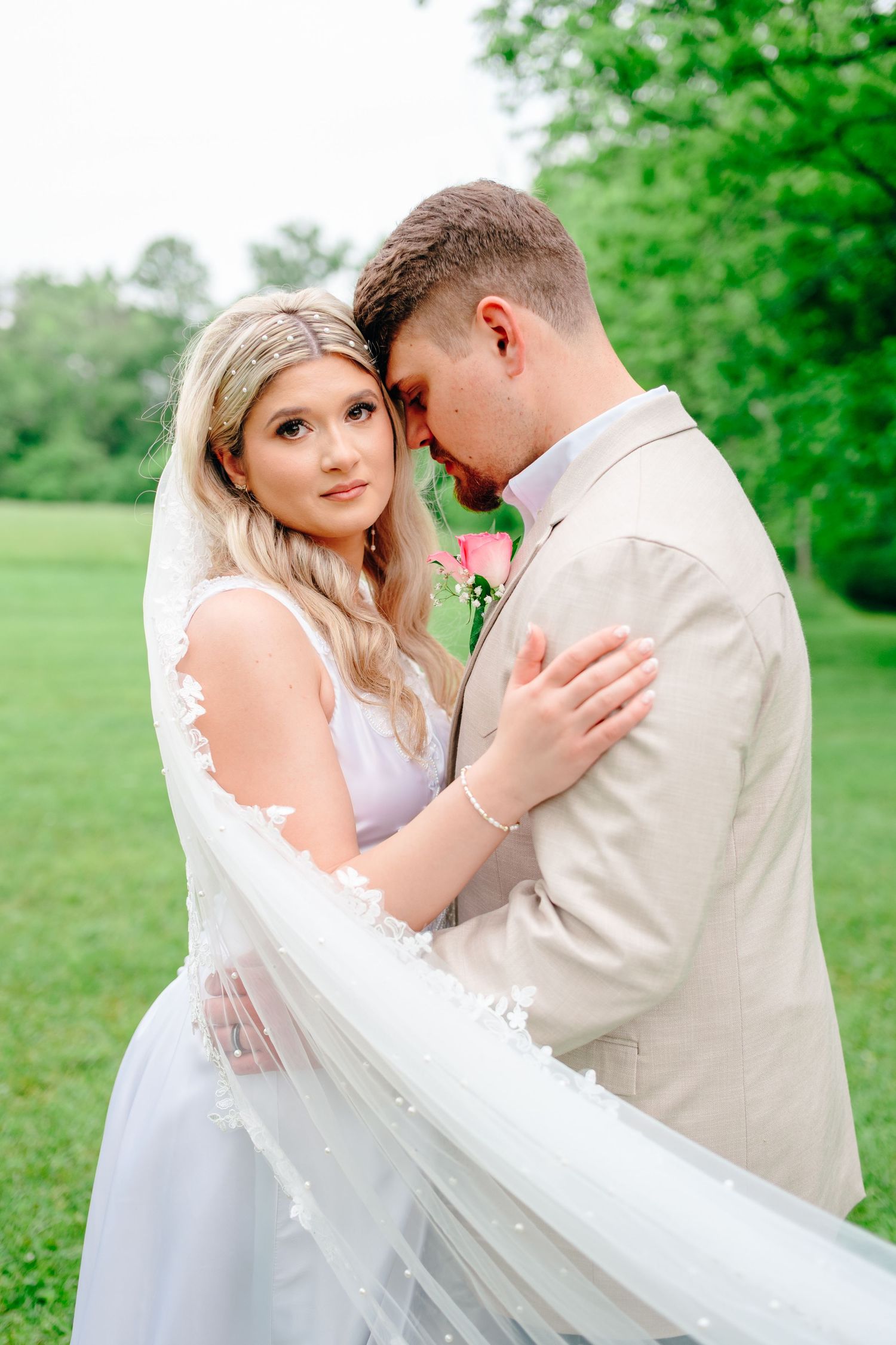 Romantic wedding couple embraces in a lush green garden setting wearing white dress and beige suit.