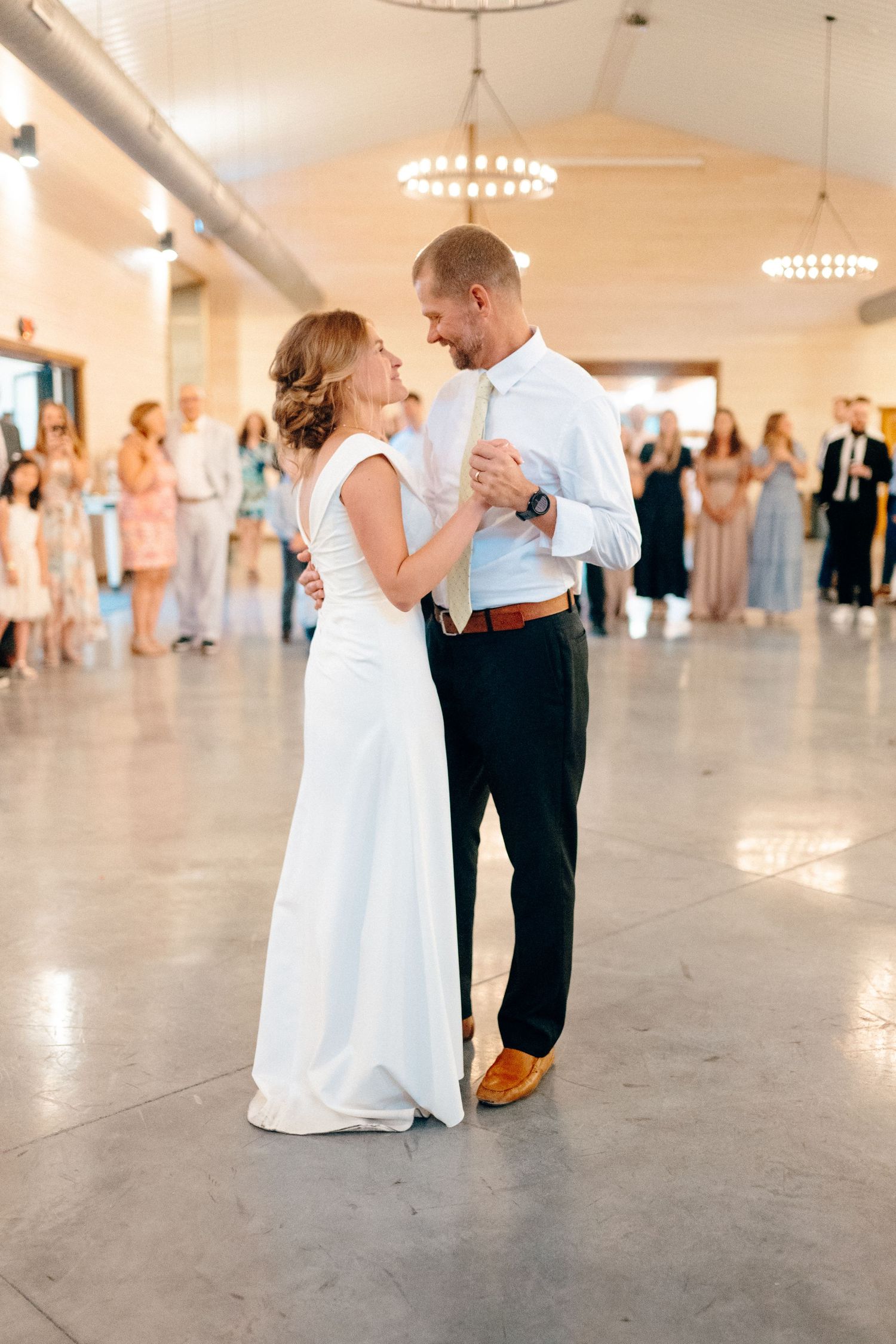 Newlyweds share their first dance in an elegant venue with crystal chandeliers and watching guests.