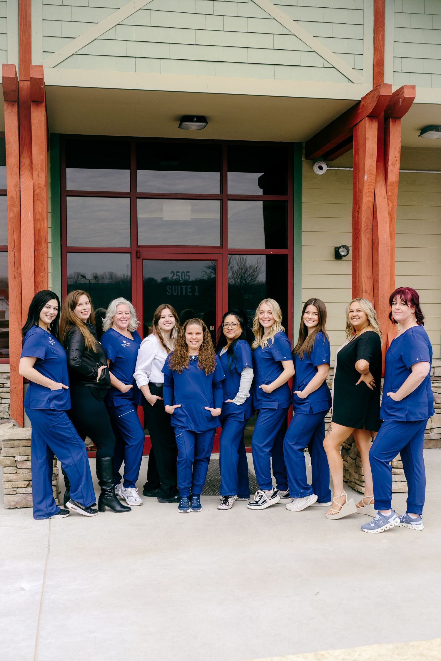 Group photo of healthcare workers in blue scrubs lined up against a building exterior.