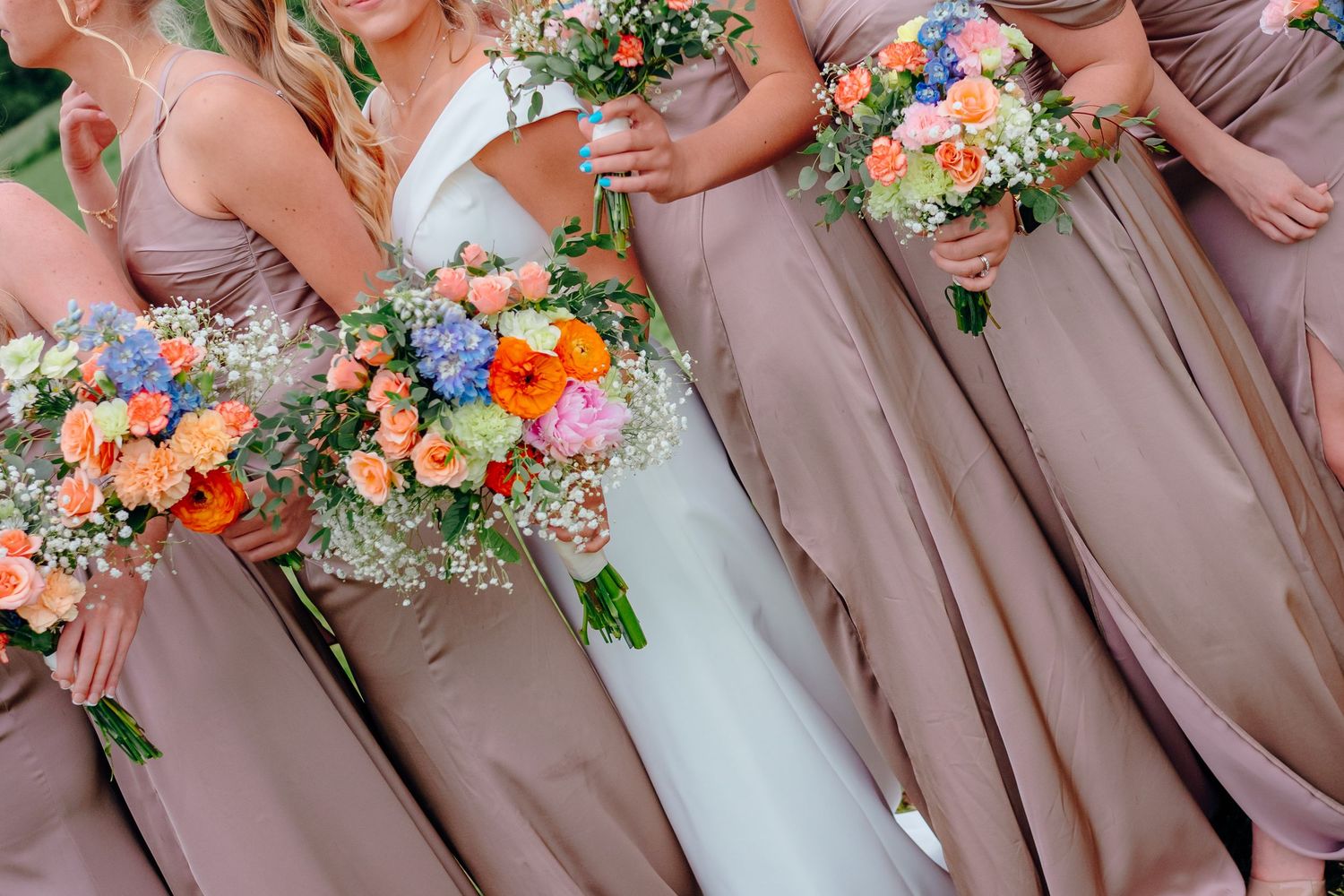 Wedding party members hold vibrant orange and pink bouquets while wearing mauve bridesmaid dresses.