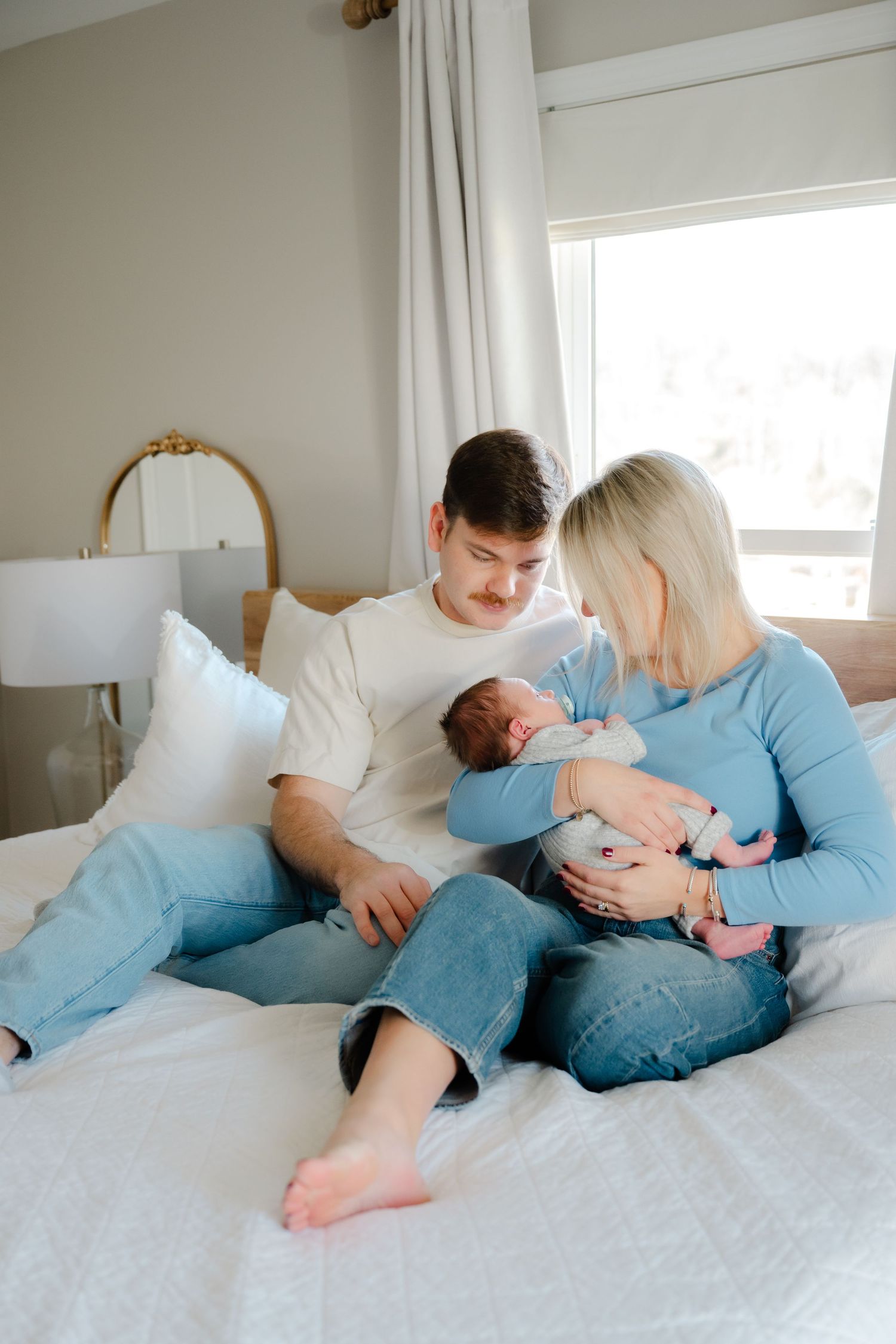 Family cuddling together on white bed wearing blue and white clothing.