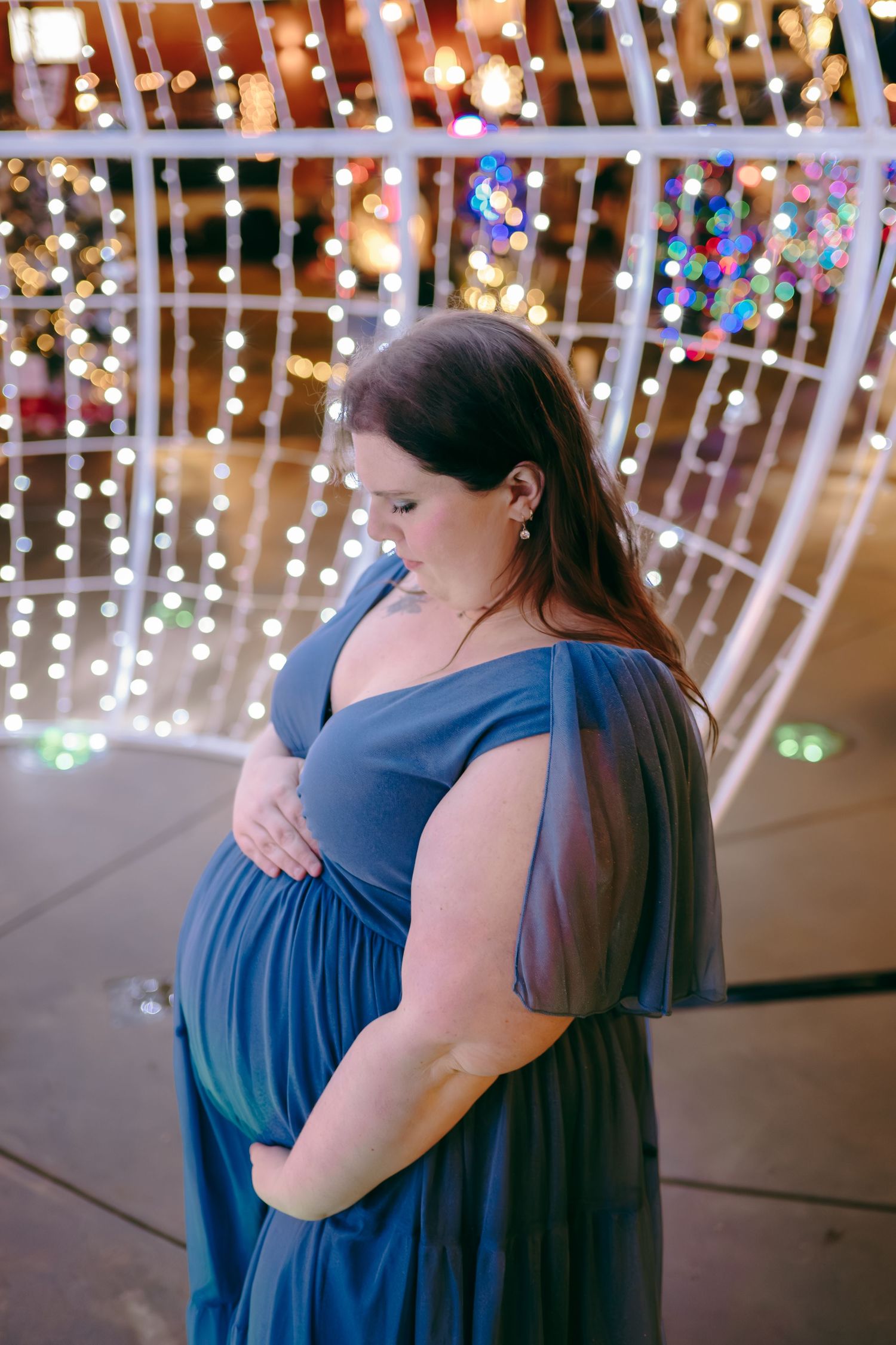 Maternity photos with twinkling lights showing embraces in a blue dress.