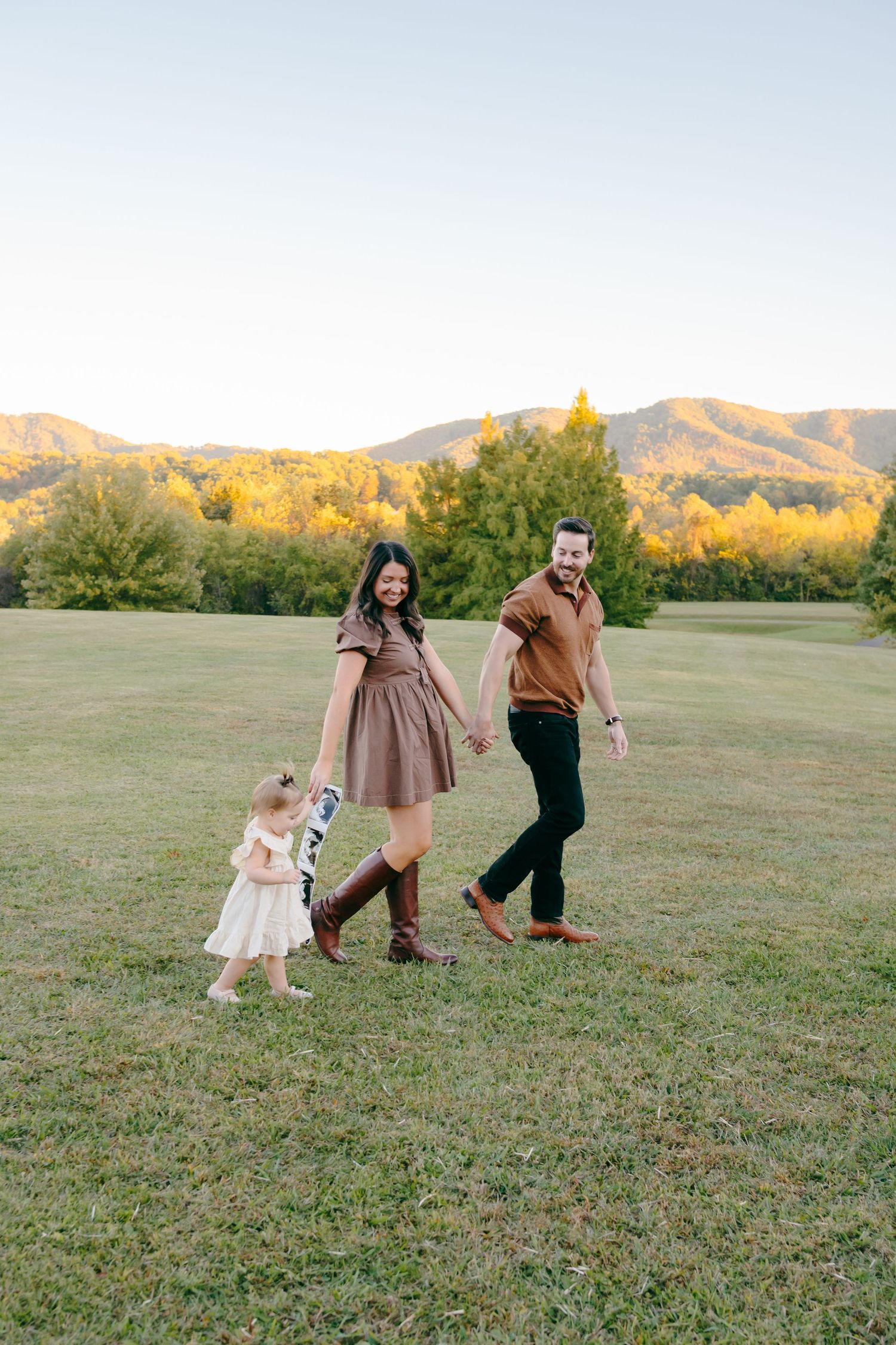 A family walks together across a grassy field with mountains visible in the background.