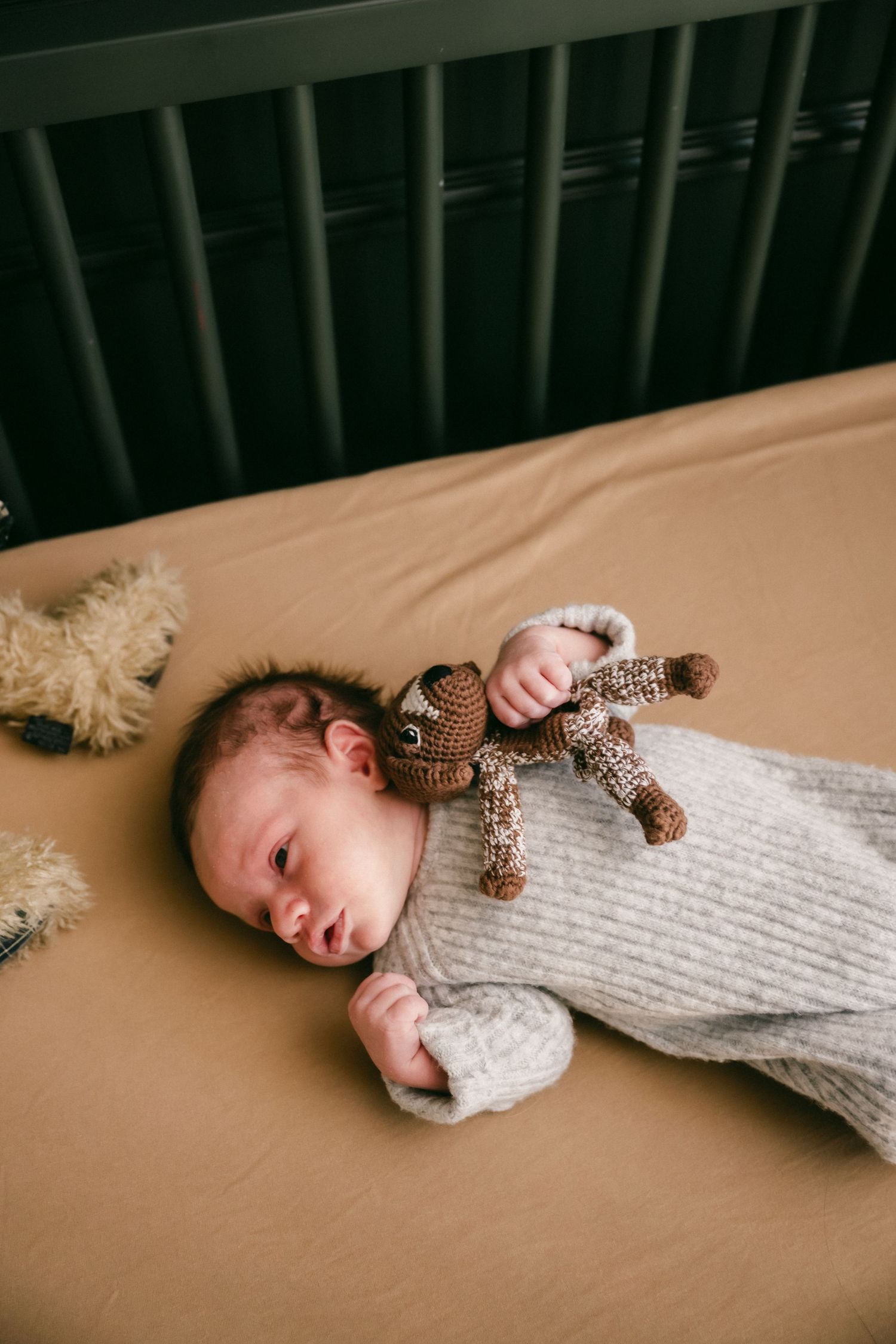 Baby in white knit sweater lies on beige surface with decorative bow.