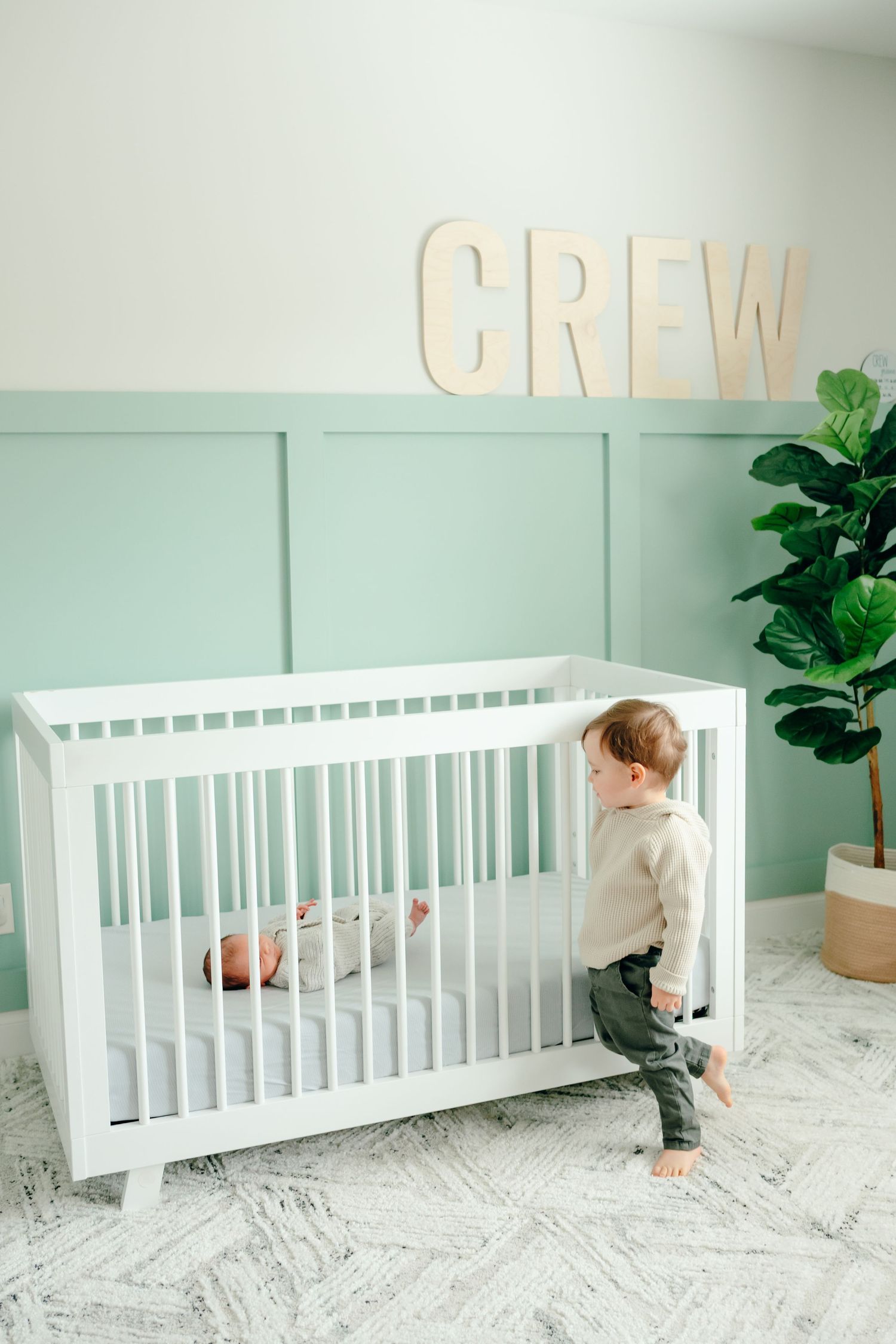White nursery with crib features wooden letters spelling a name on mint green wall.