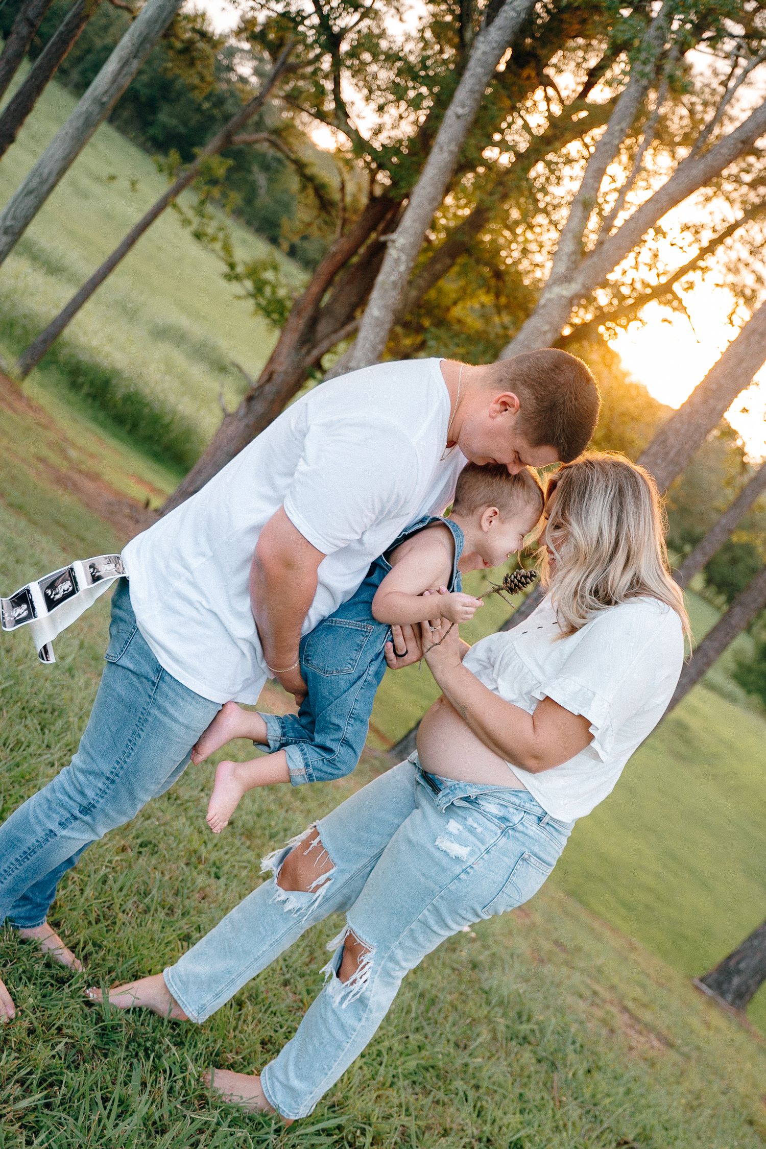 Family embracing in outdoor setting with pine trees during sunset.