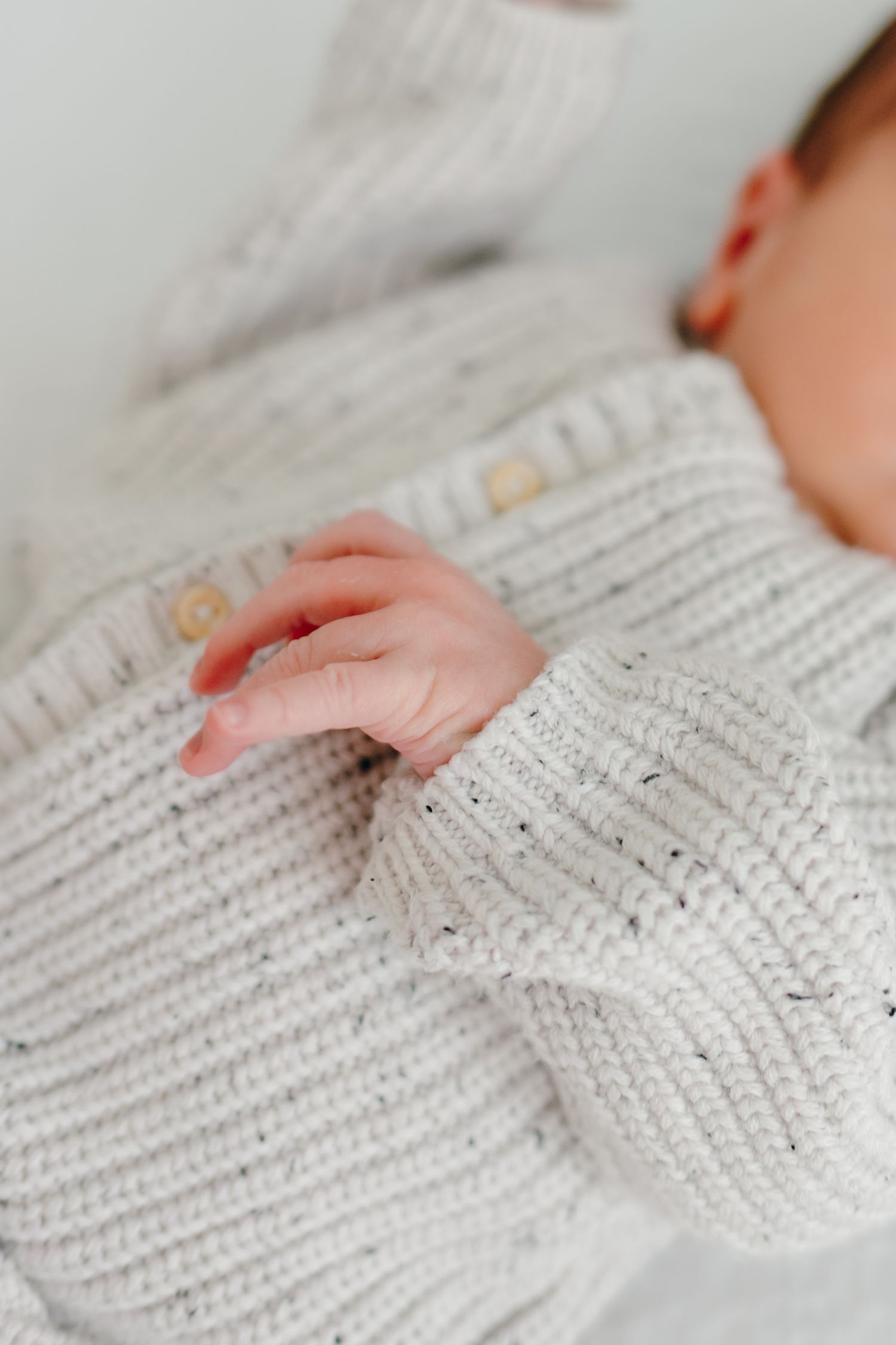 Close up detail of white knitted sweater texture and tiny hands.