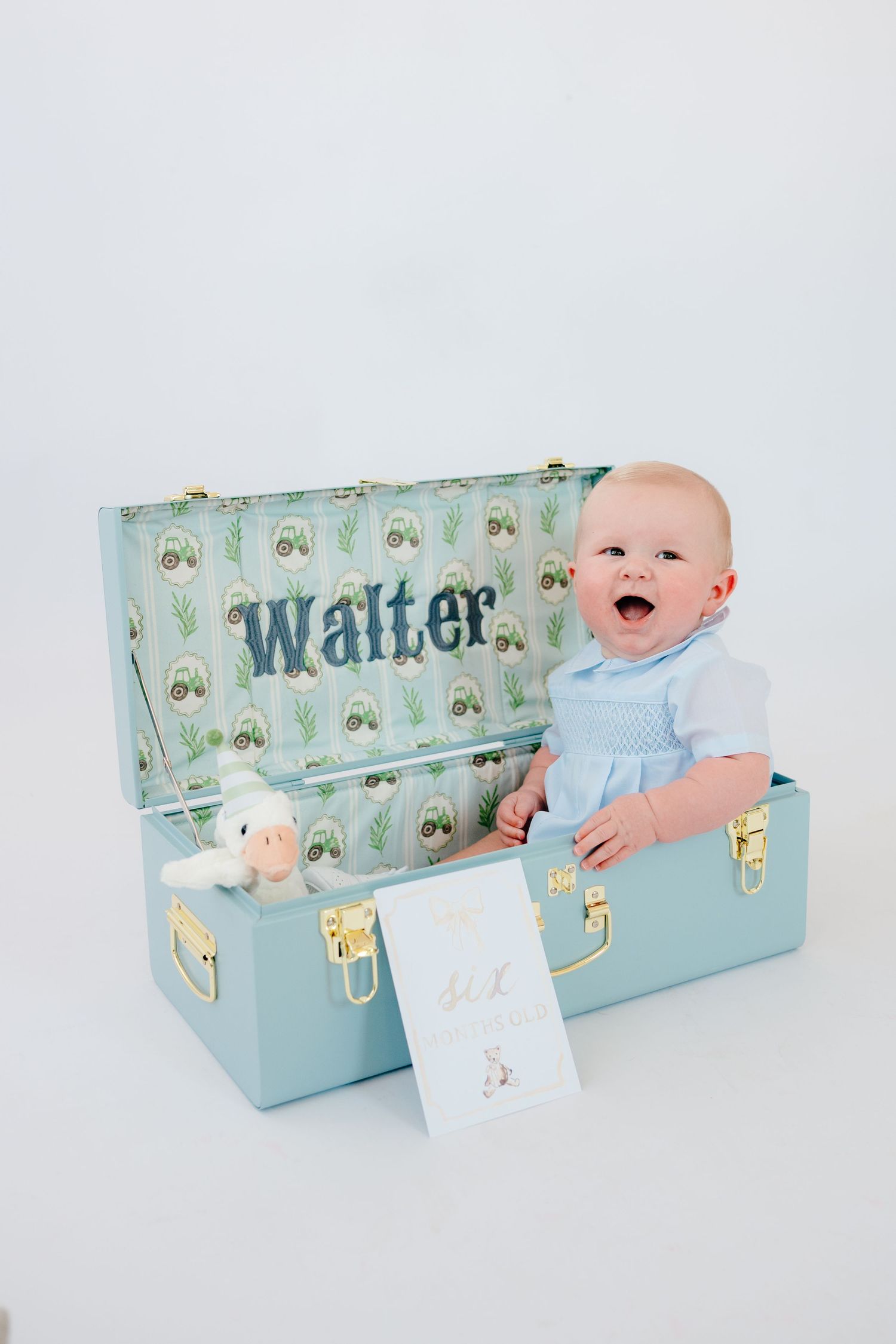 Baby lying next to decorative blue box with 'Walter' text and nursery patterns.