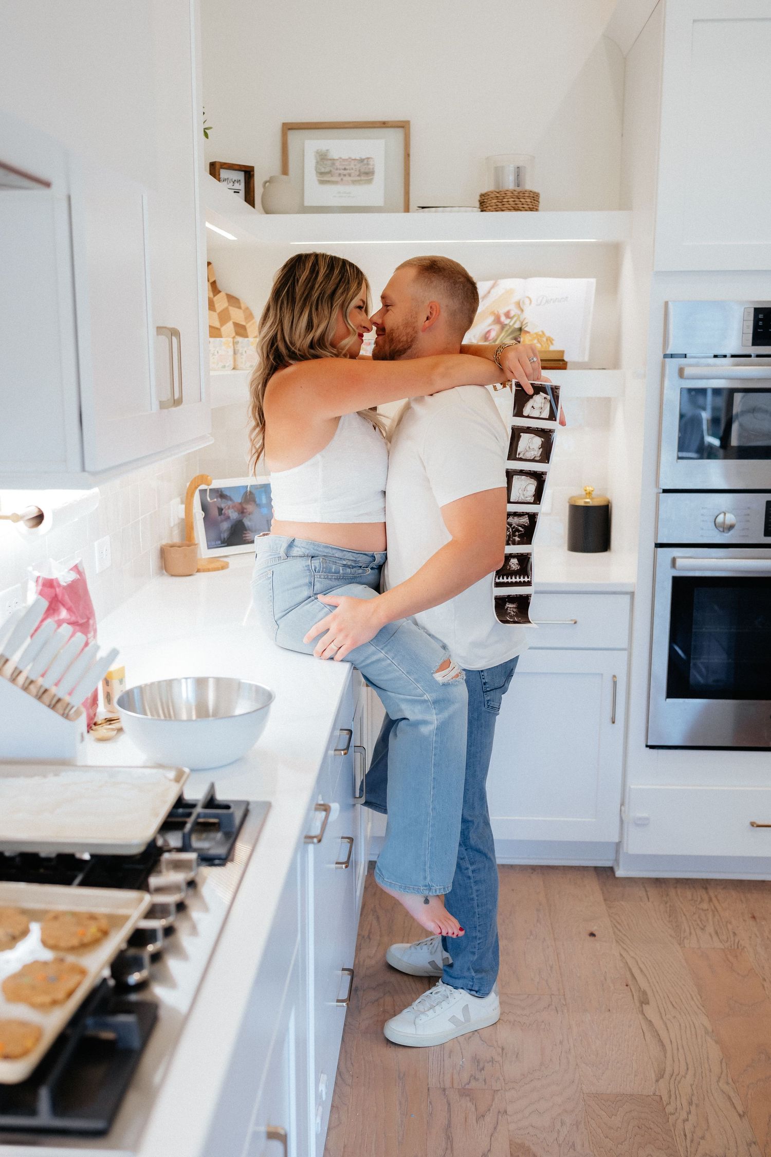 Couple sharing joyful moments in their modern white kitchen while holding ultrasound images.