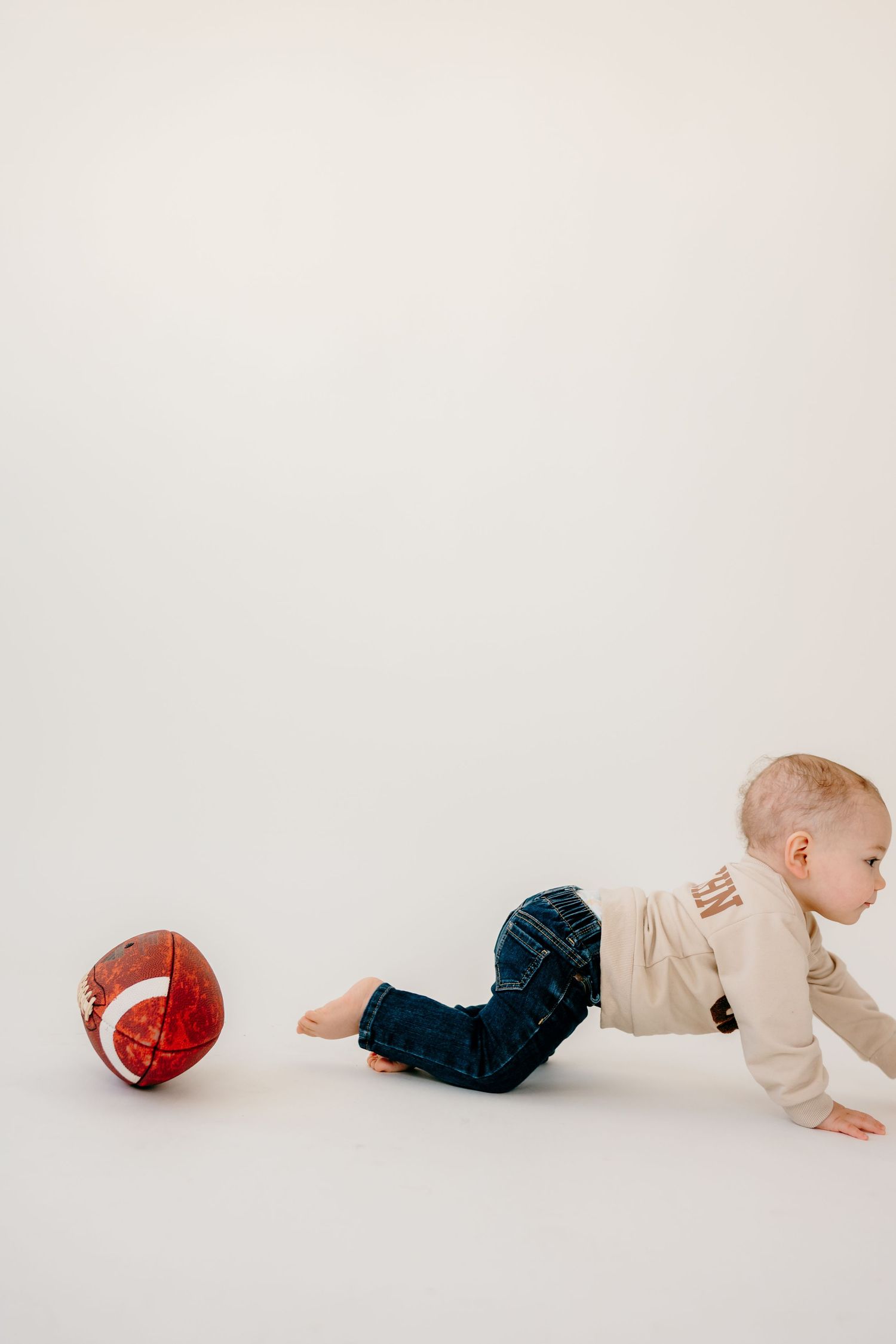 Baby crawls on white floor while chasing a red ball.