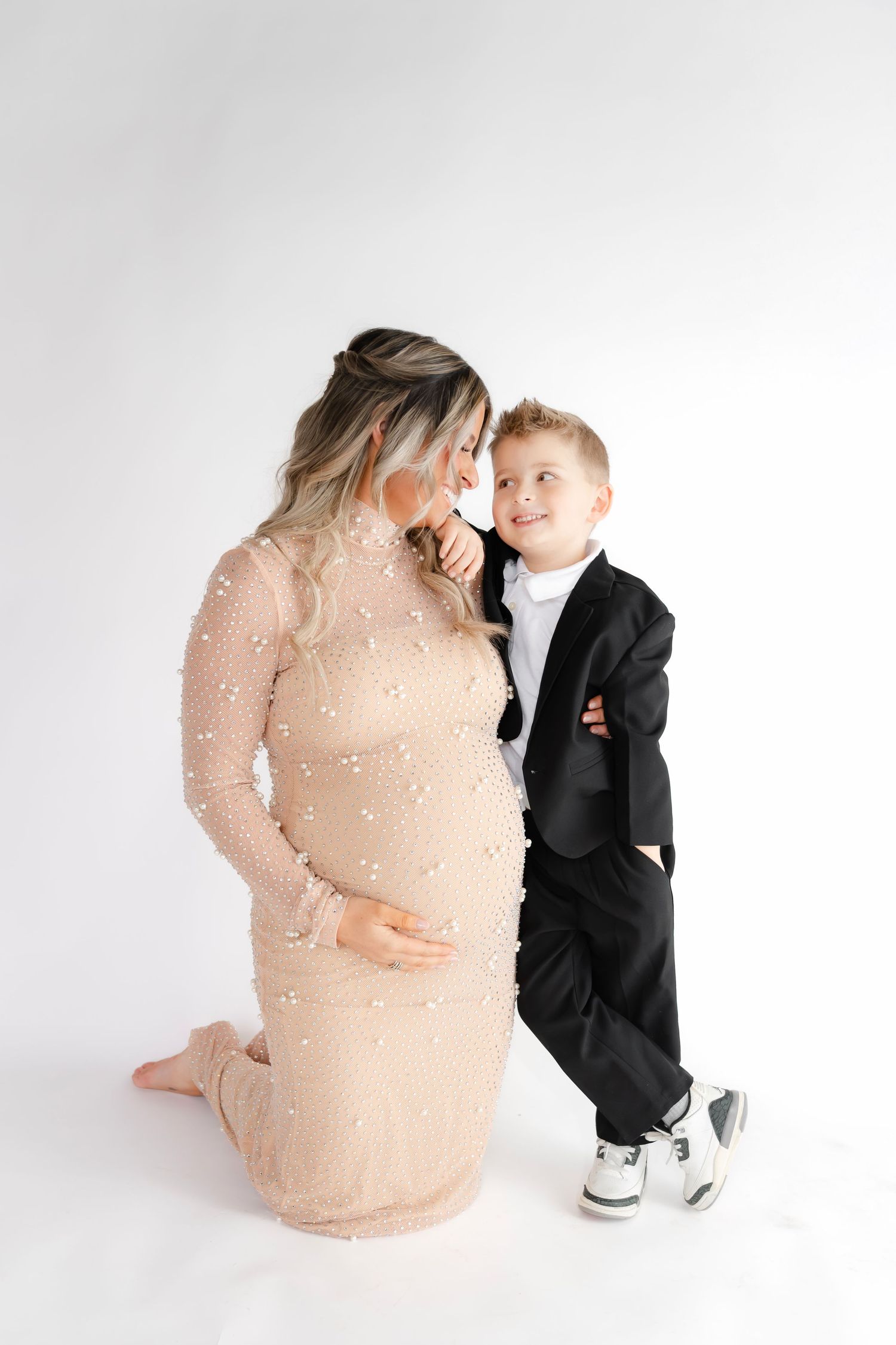Candid maternity session showing tender moments between mother and young son in formal wear.