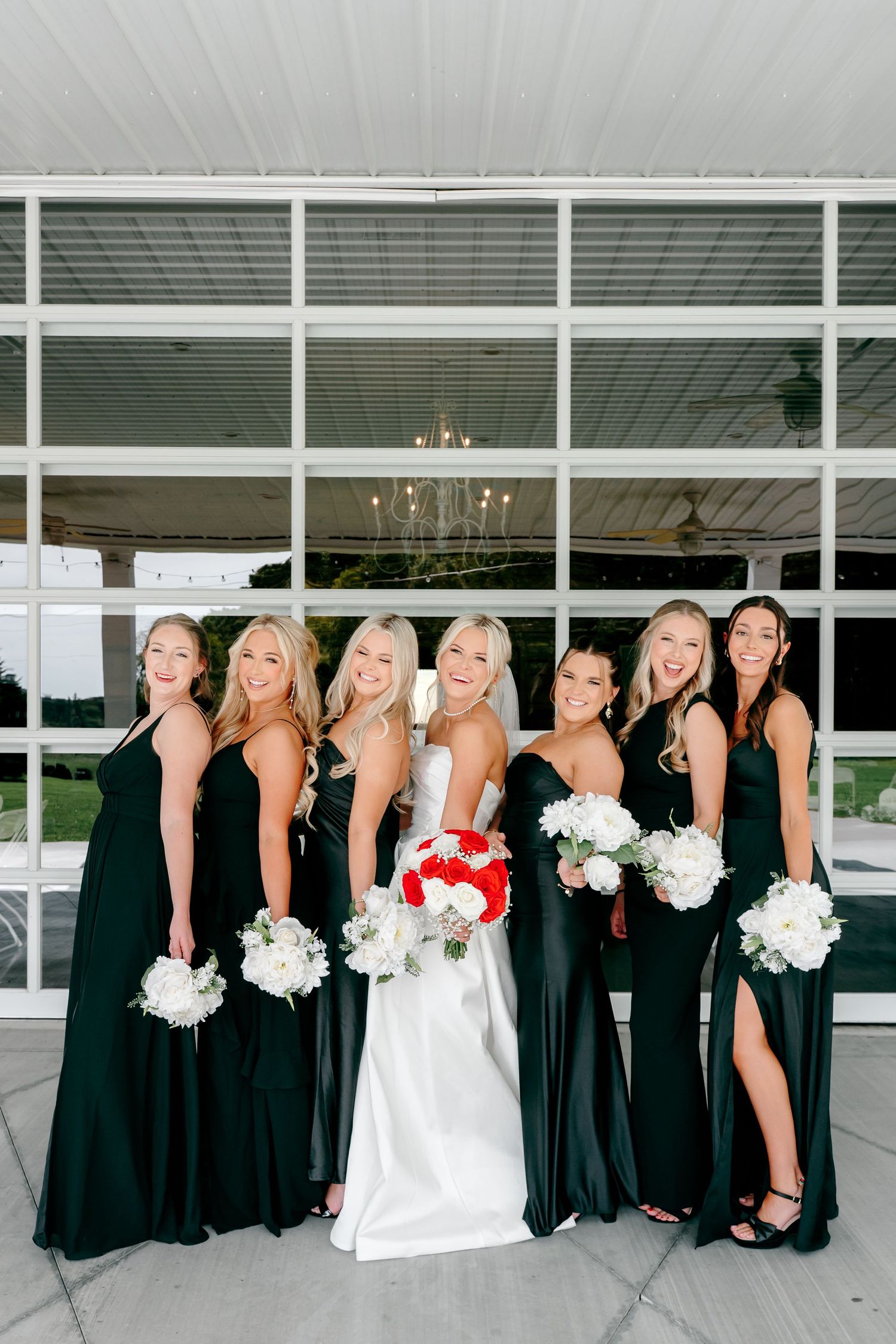 Bridal party in elegant black dresses and white gowns pose together against modern architecture.