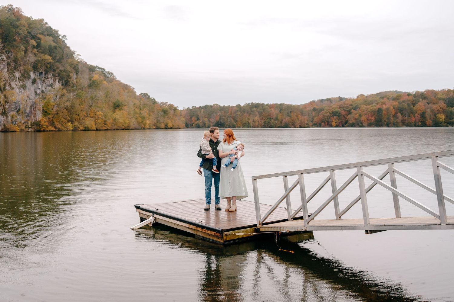 A couple shares a romantic moment on a wooden dock overlooking a serene lake surrounded by autumn foliage.