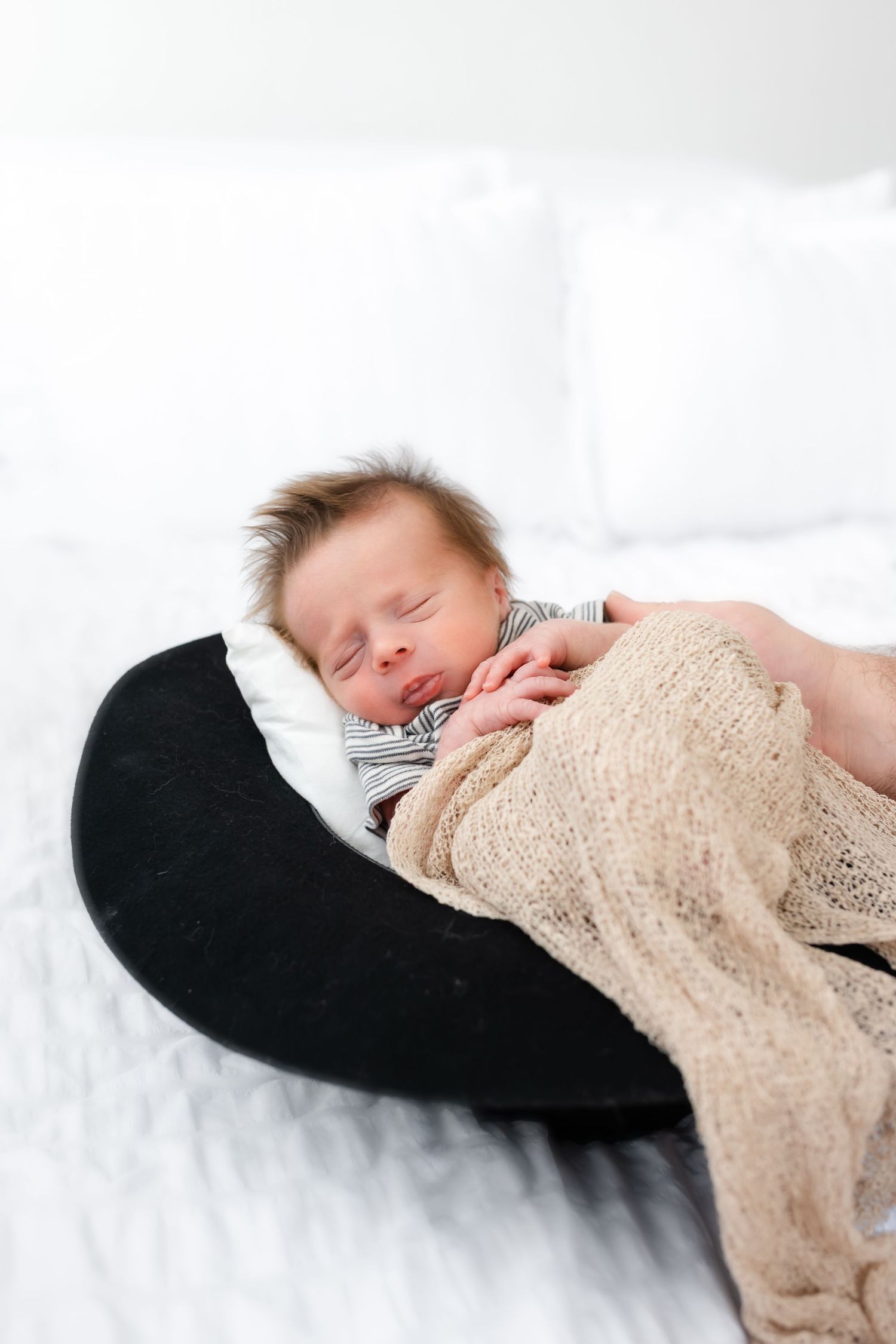 A sleeping baby wrapped in a beige lace blanket rests peacefully on white bedding.