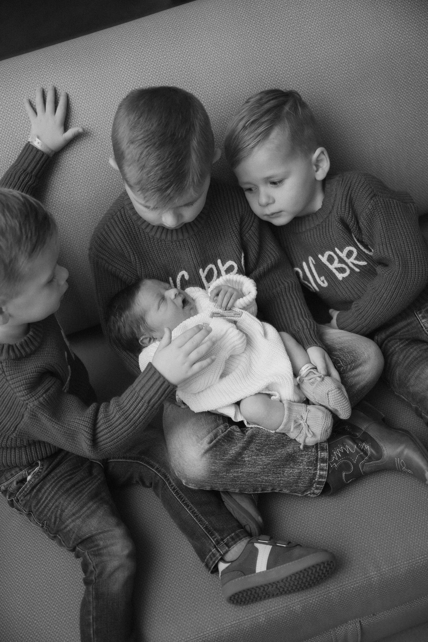 Black and white photos of siblings bonding with a newborn baby on a couch.