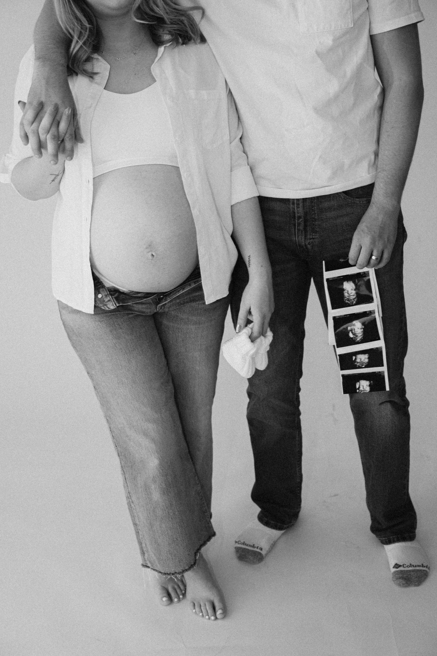 Black and white photo showing legs of people walking together while holding ultrasound photos.