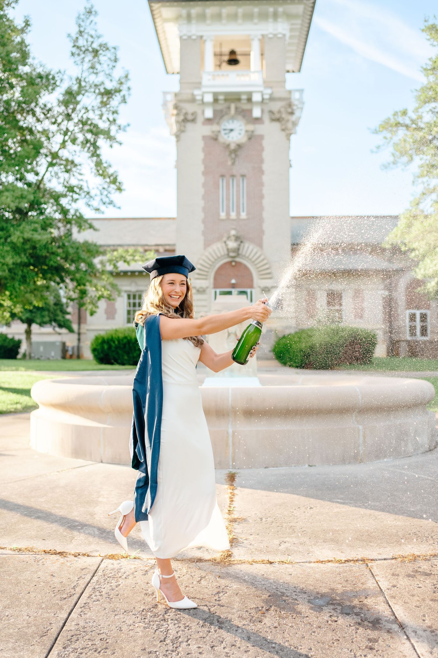 Graduate celebrates with champagne spray in front of historic campus building.