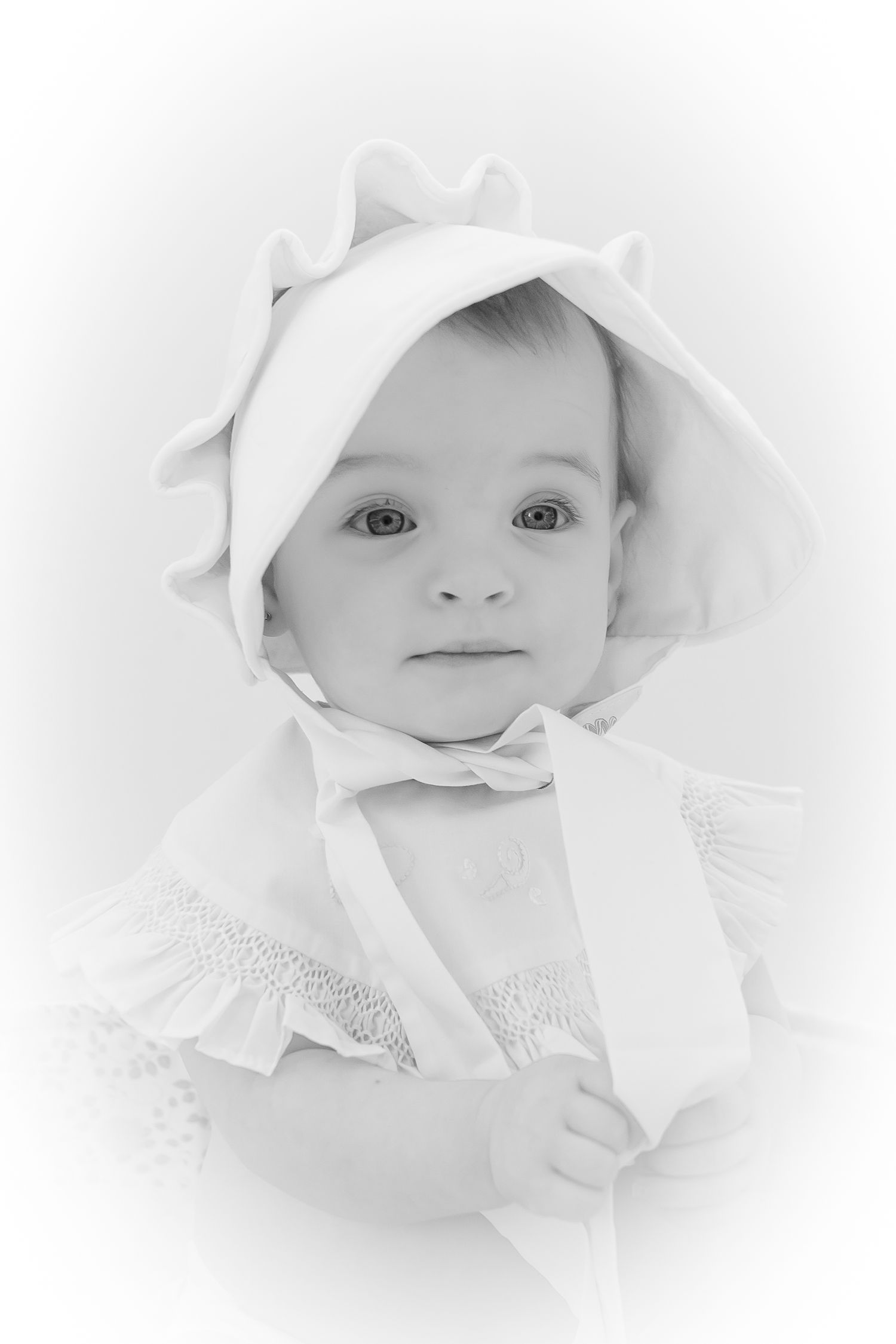 Ethereal high-key portrait of a baby's face emerging from soft white fabric in a dreamy artistic style.