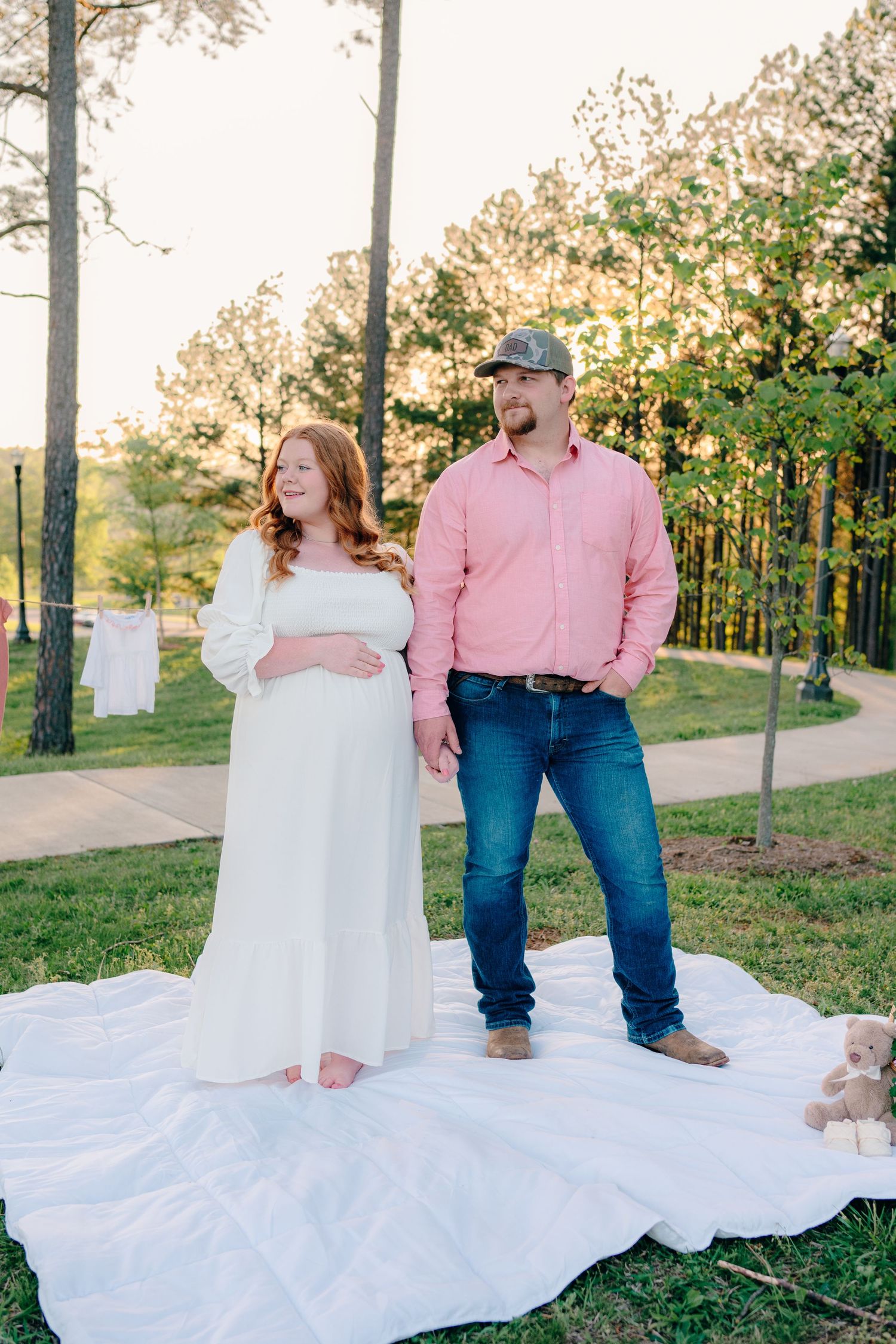 A couple poses on a white blanket during an outdoor maternity session.