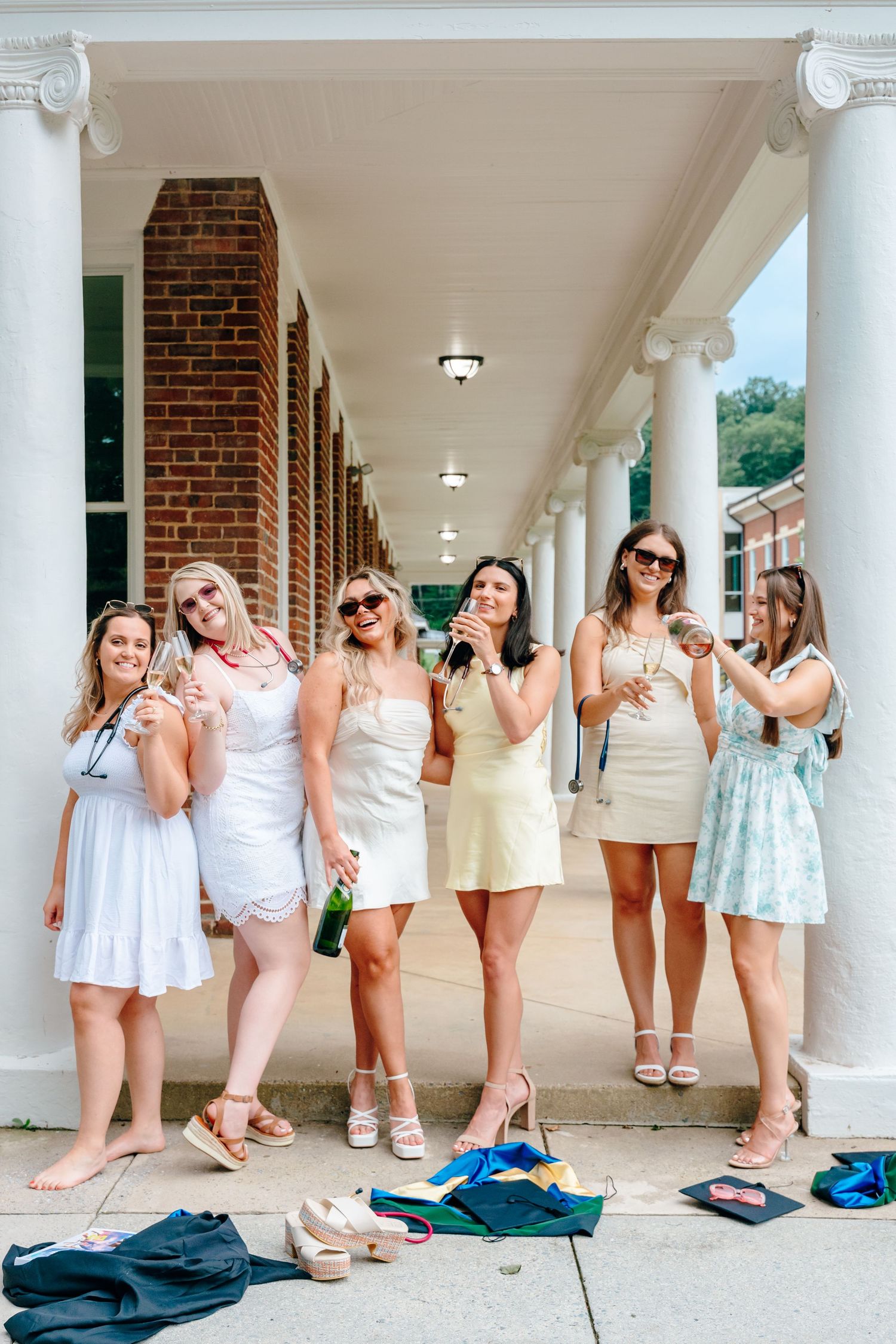 Group poses playfully in white dresses under columned portico.