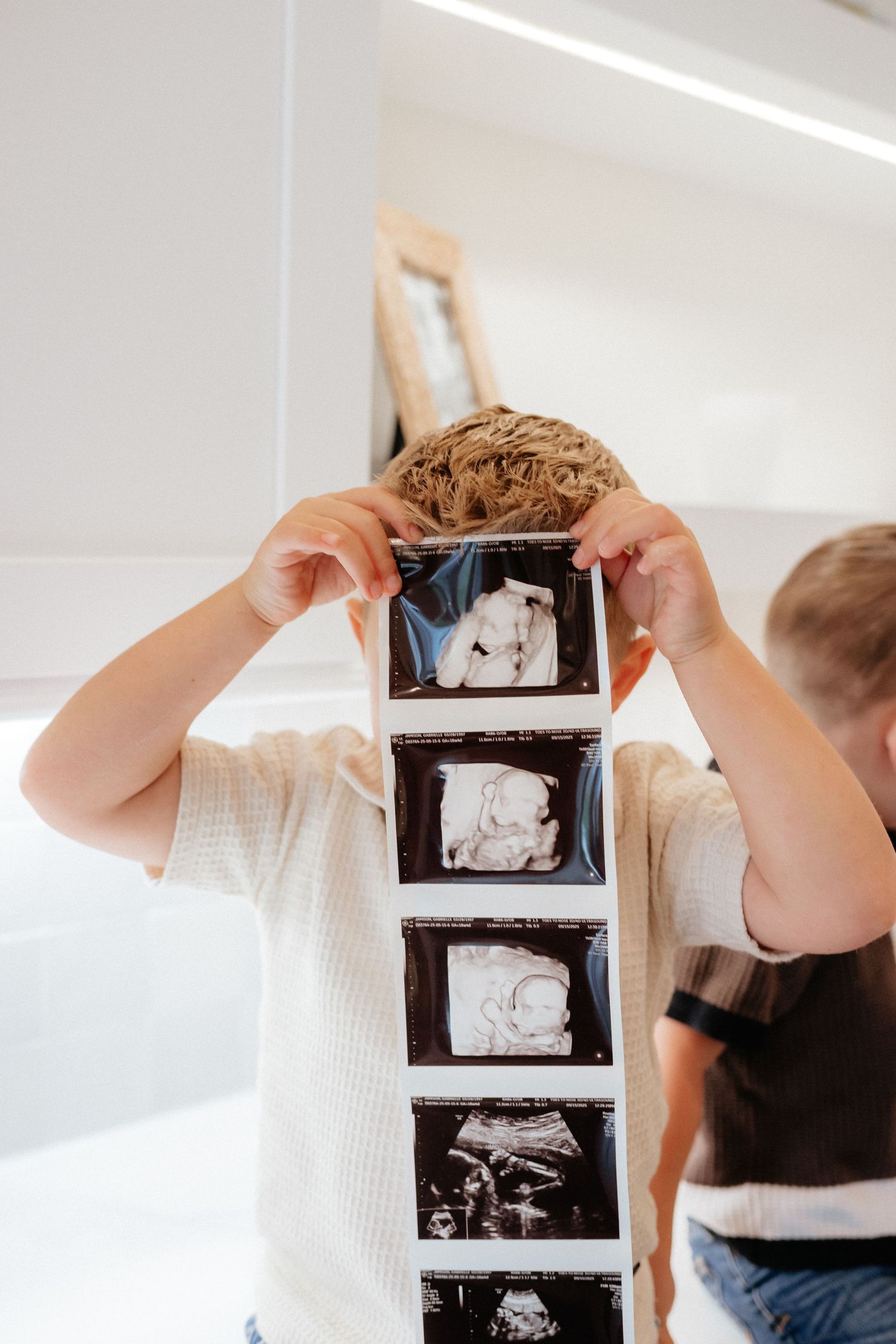 Someone holds up a strip of ultrasound photos in a bright white kitchen.