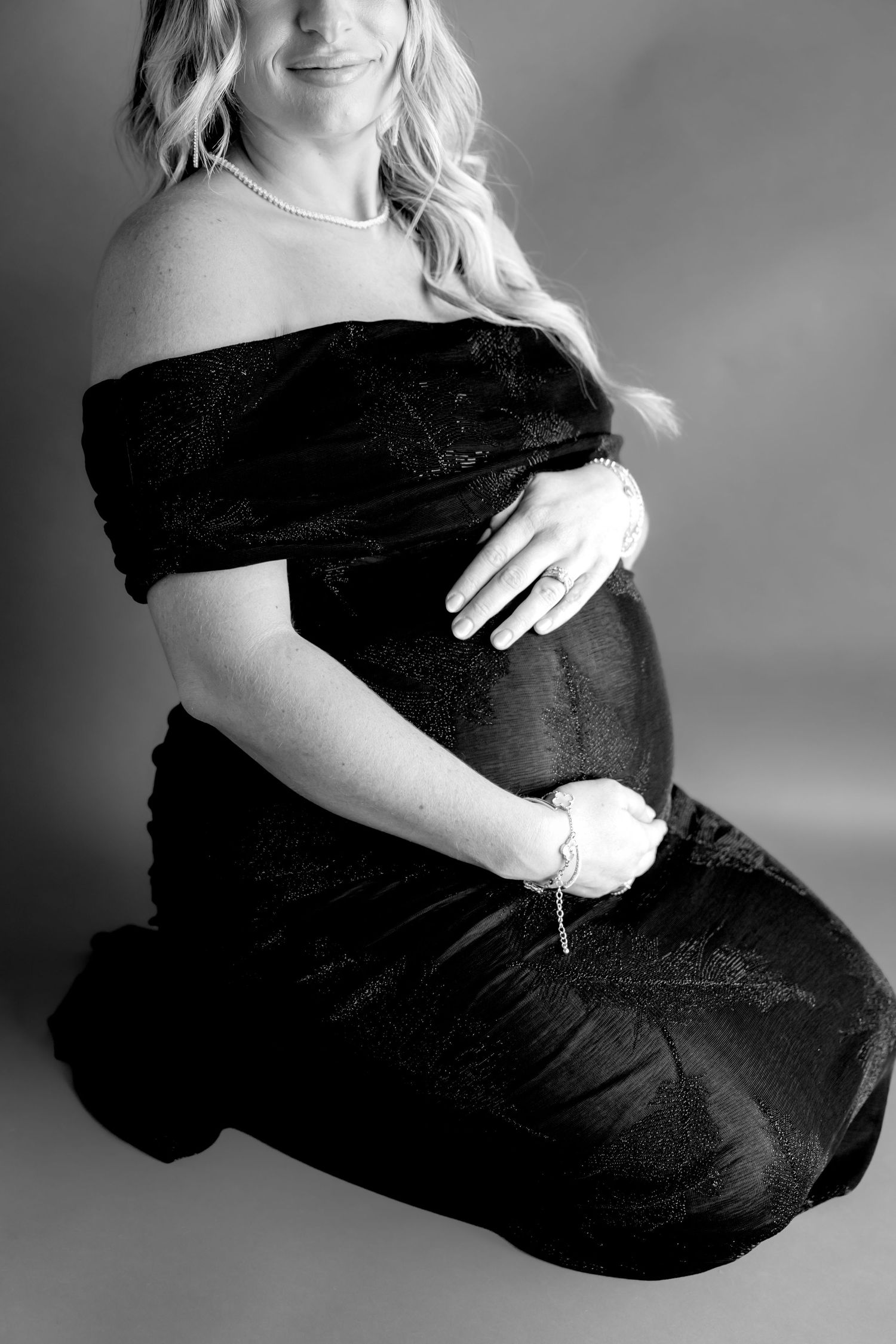 Black and white maternity portrait showing woman in off-shoulder dress.