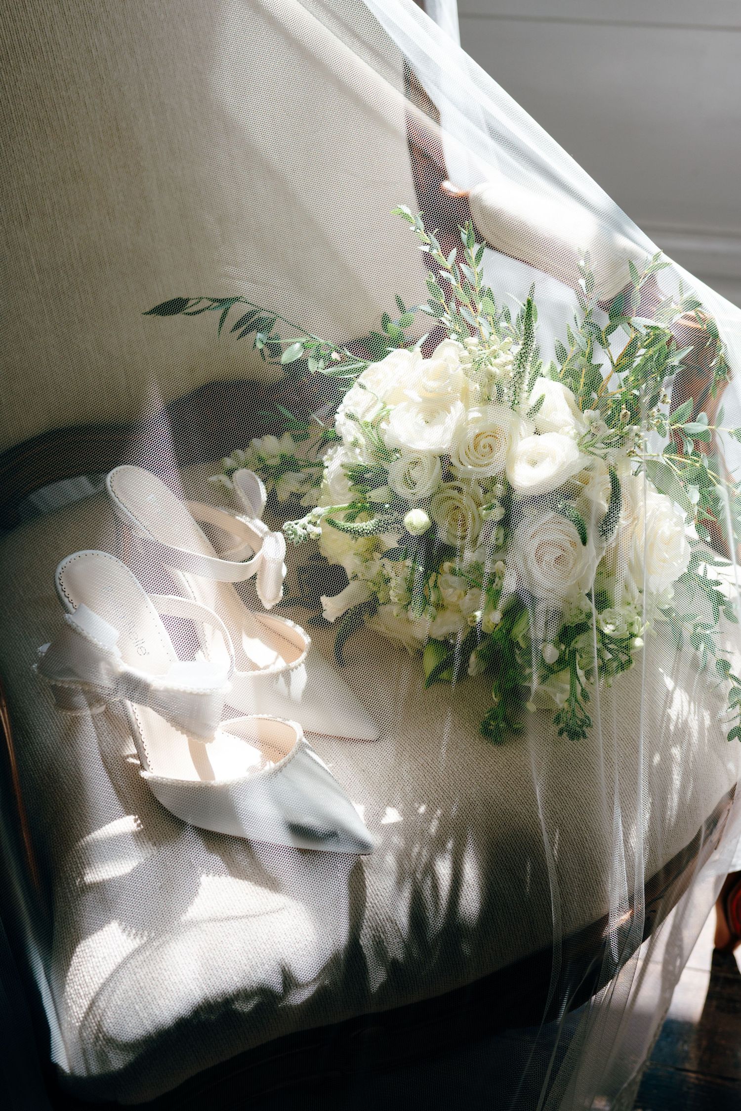 White bridal shoes and floral bouquet arranged near window with soft natural lighting.