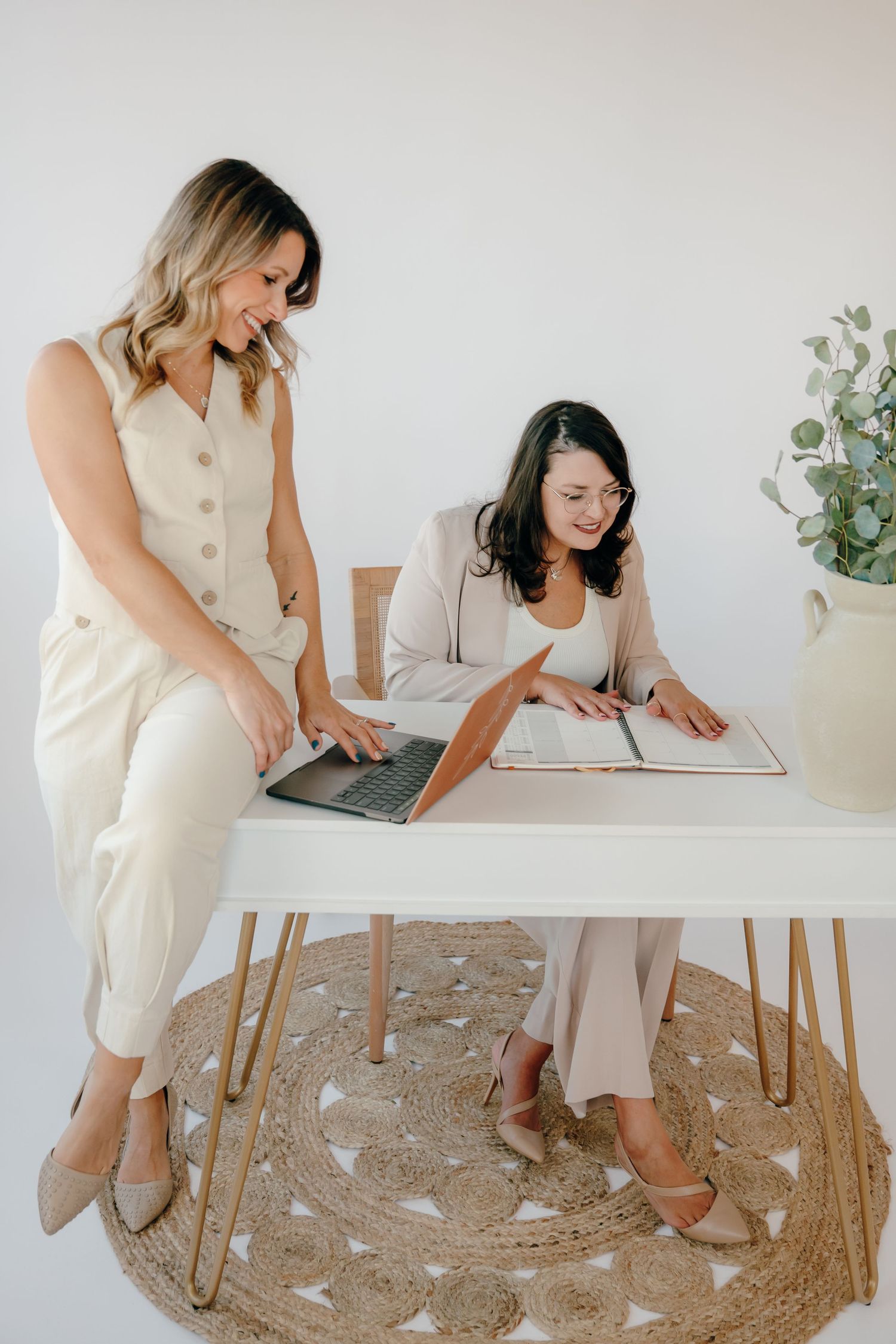 Two professionals collaborating at white desk with laptop and documents in bright minimal office setting.