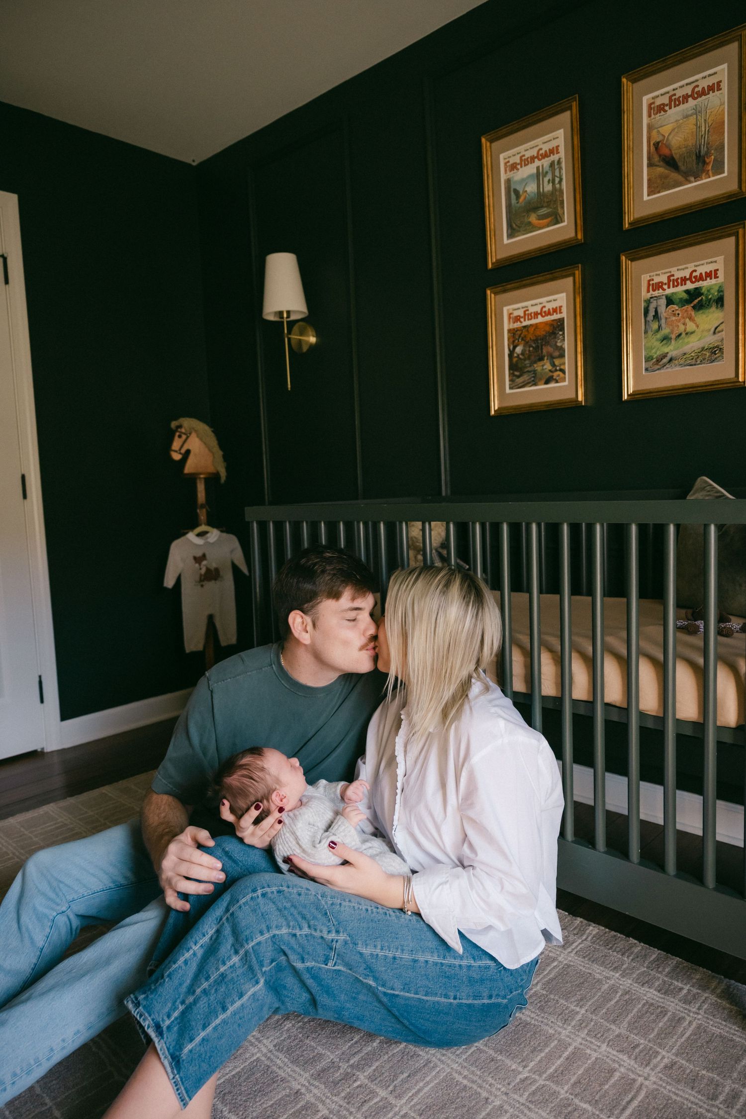 Family members sharing intimate moments near a crib in a nursery with framed artwork.