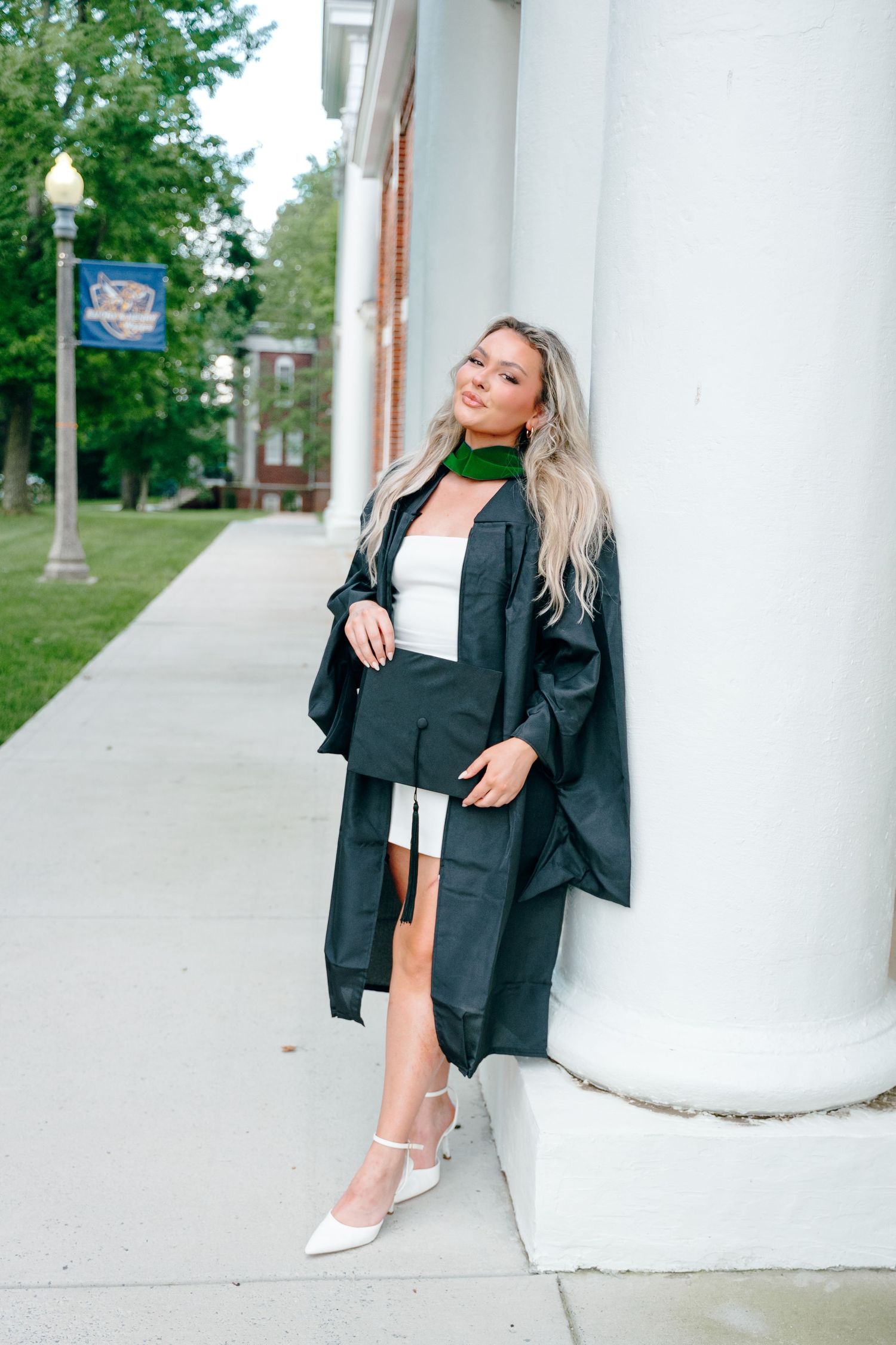 A graduation photoshoot featuring a black blazer and white dress against white columns.
