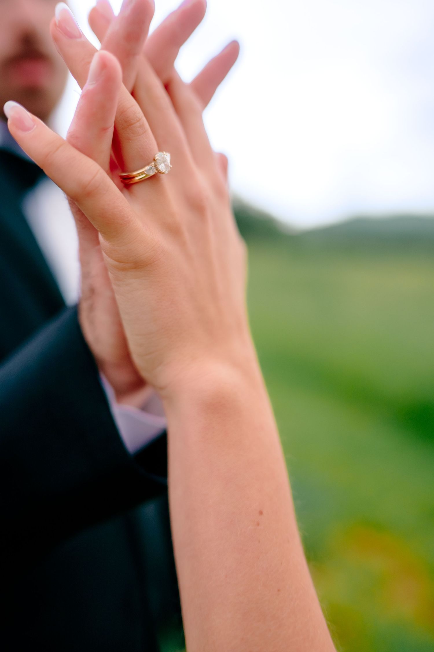 Close-up of clasped hands with wedding ring against outdoor background.