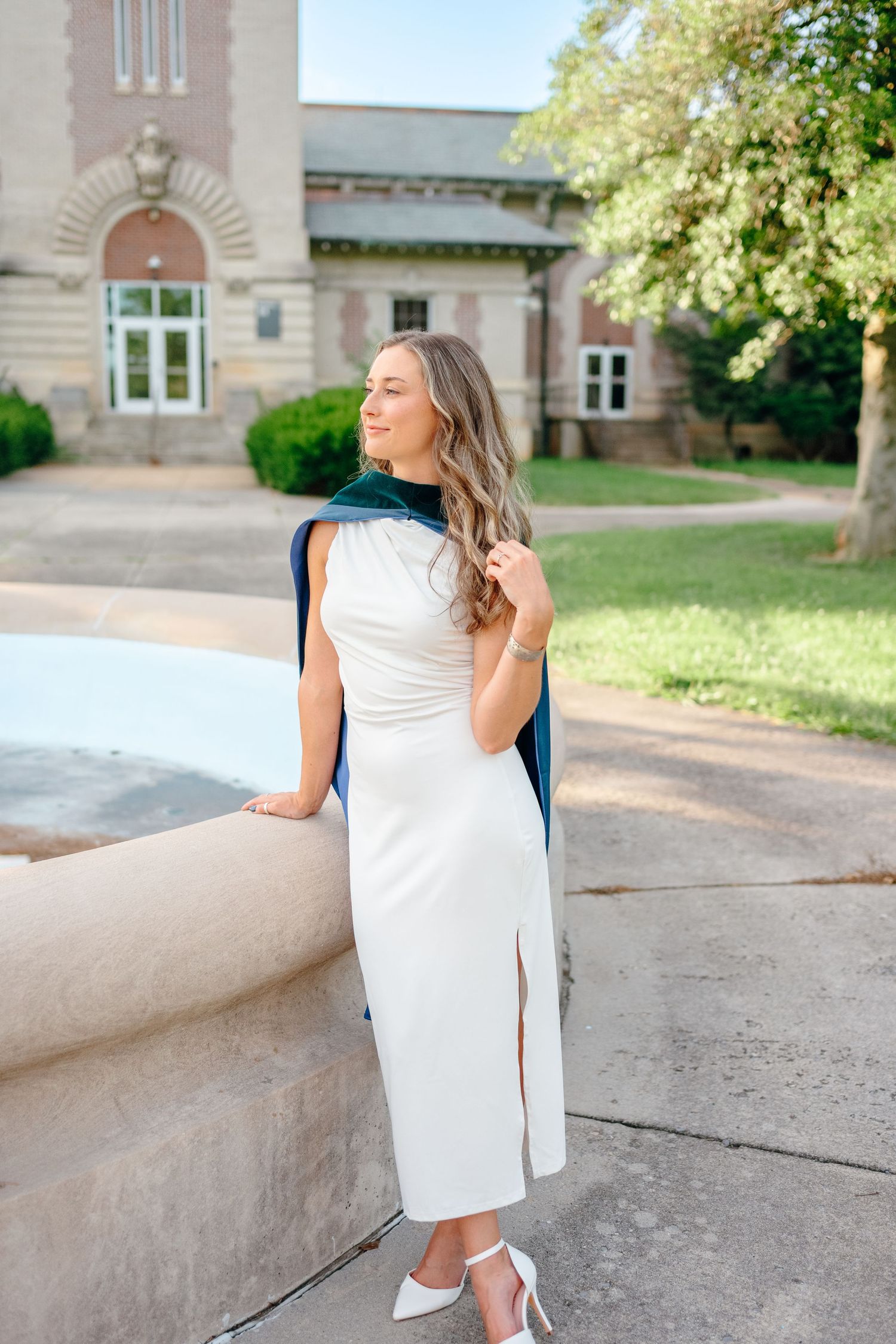 Graduate in white dress and blue stole poses against stone architecture.