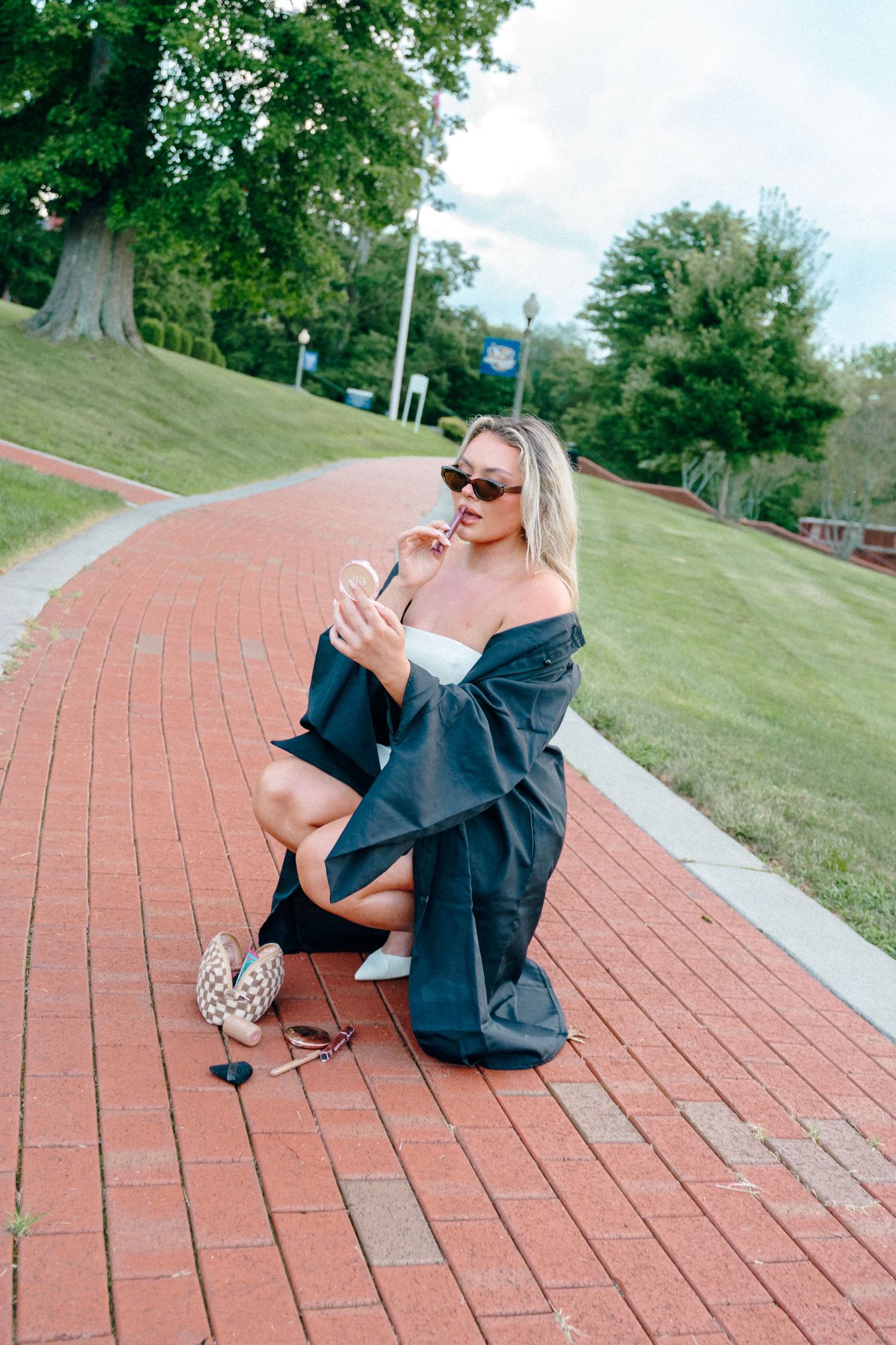 Graduate in black gown sits on brick pathway during photo session.