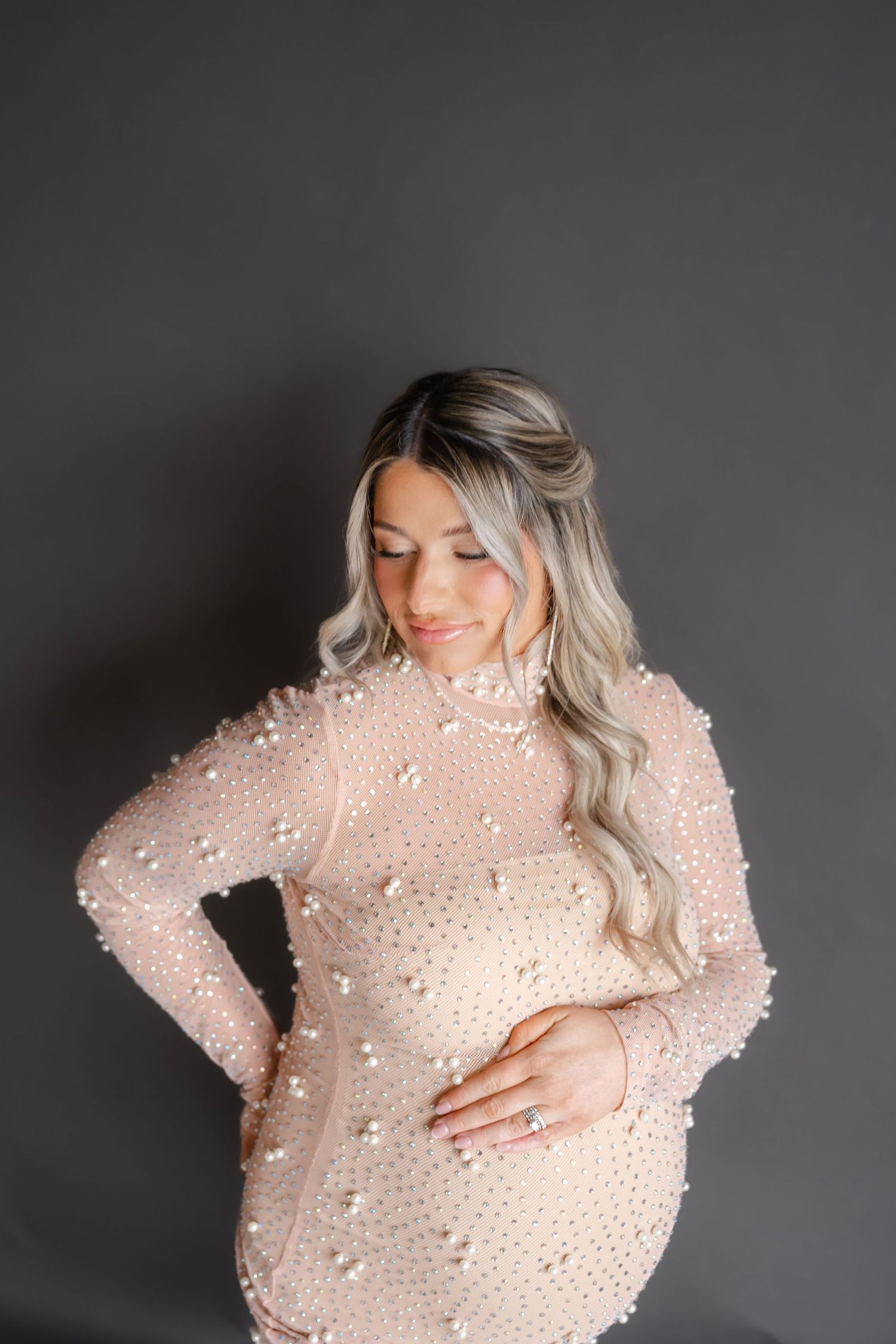Maternity photoshoot featuring a delicate pink beaded gown against a dark background.