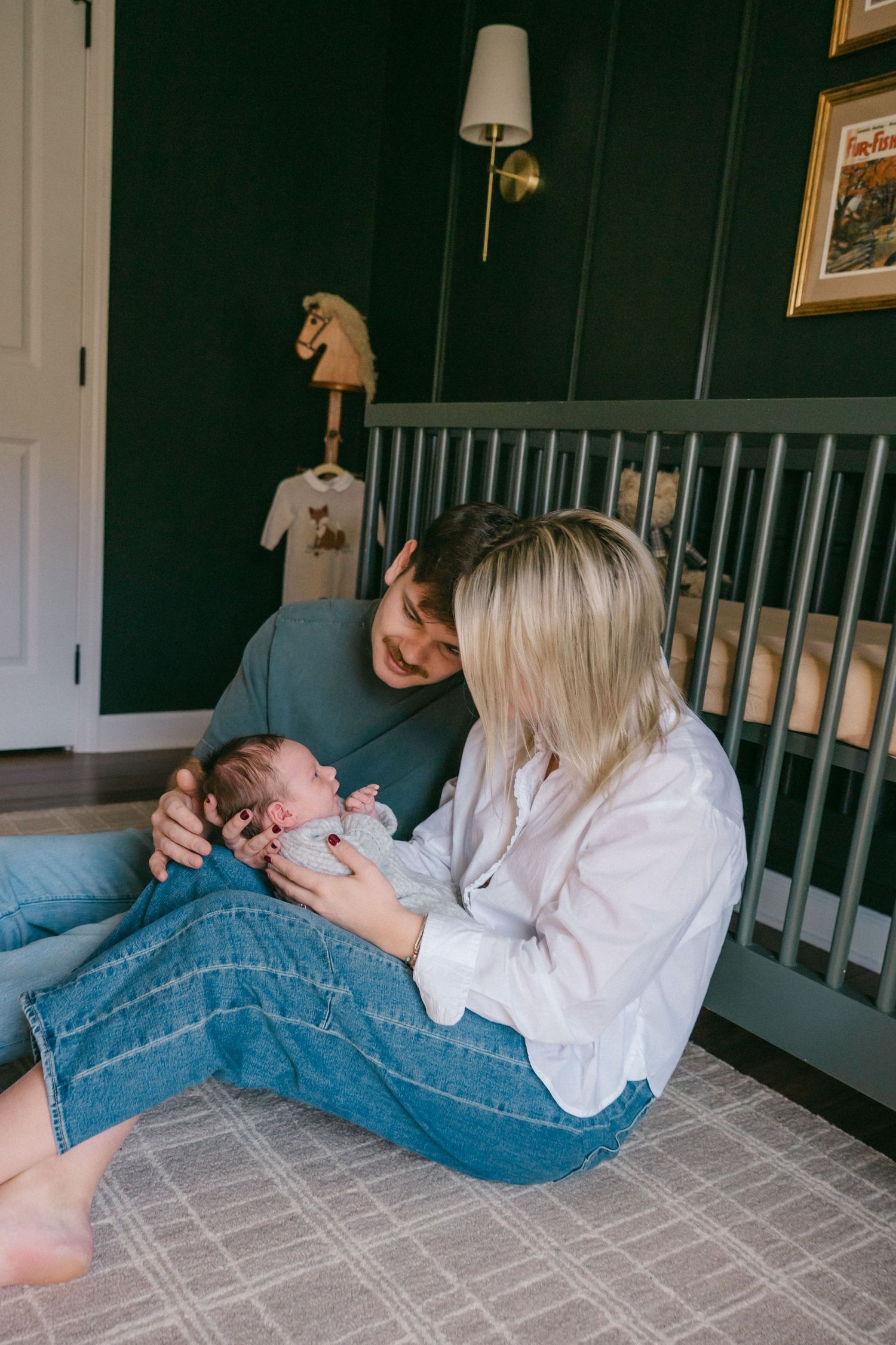 People sharing tender moments while lying on a carpeted floor near a crib.