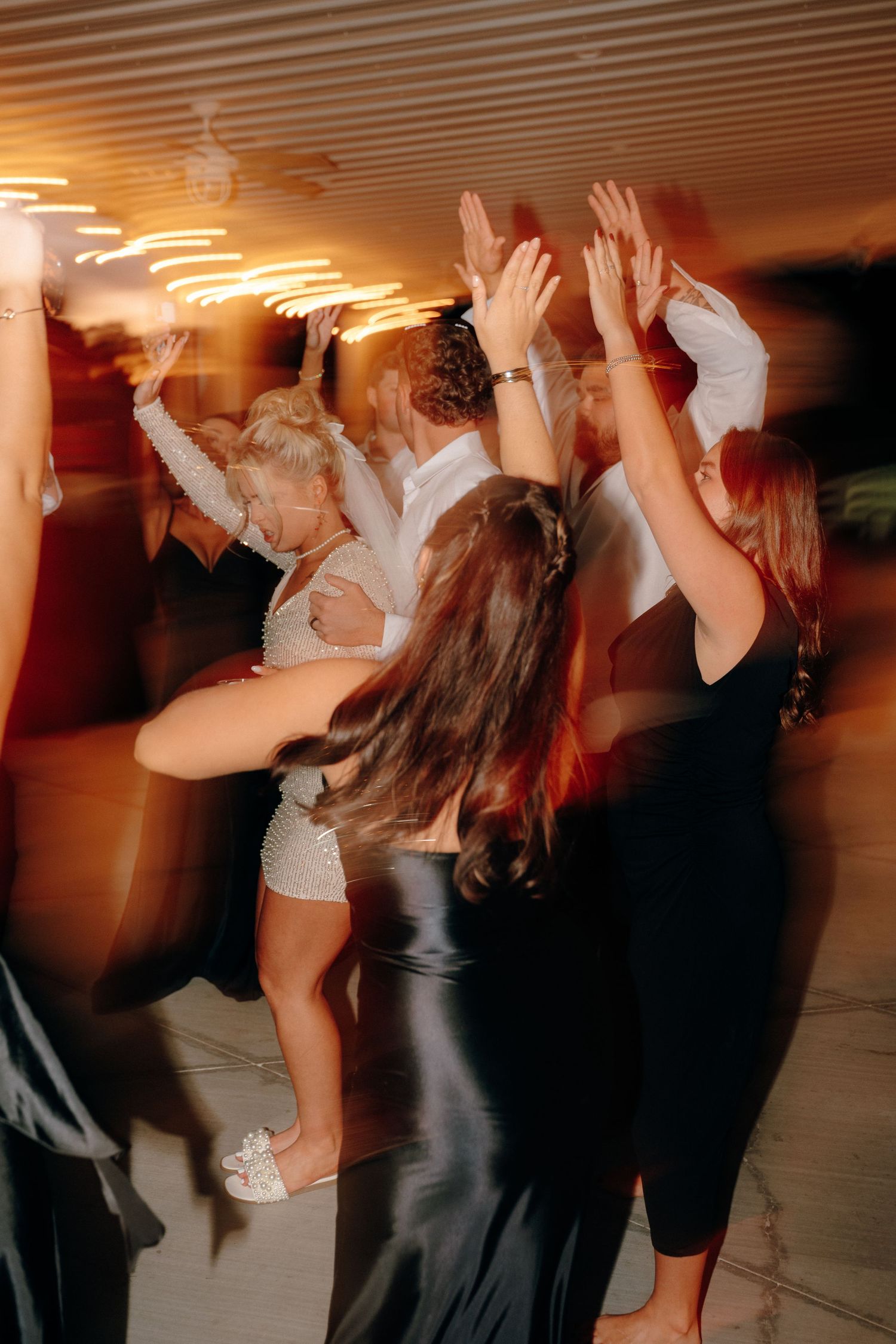 Wedding reception dance party with guests celebrating on dance floor in dimly lit venue.