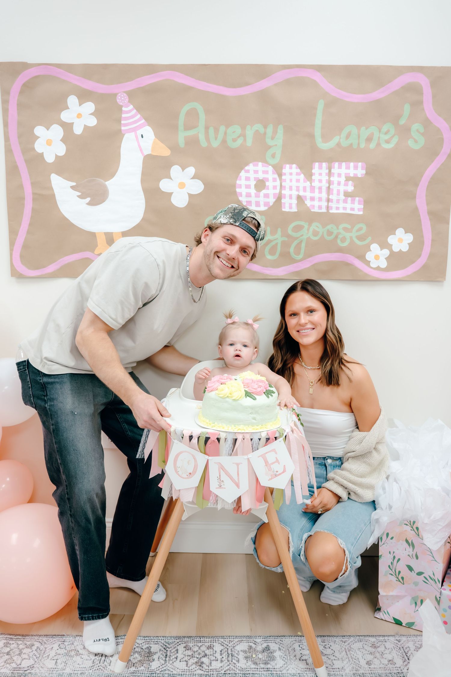 Family celebrates baby's first birthday with pink and white decorations and cake at modern farmhouse style party setup.