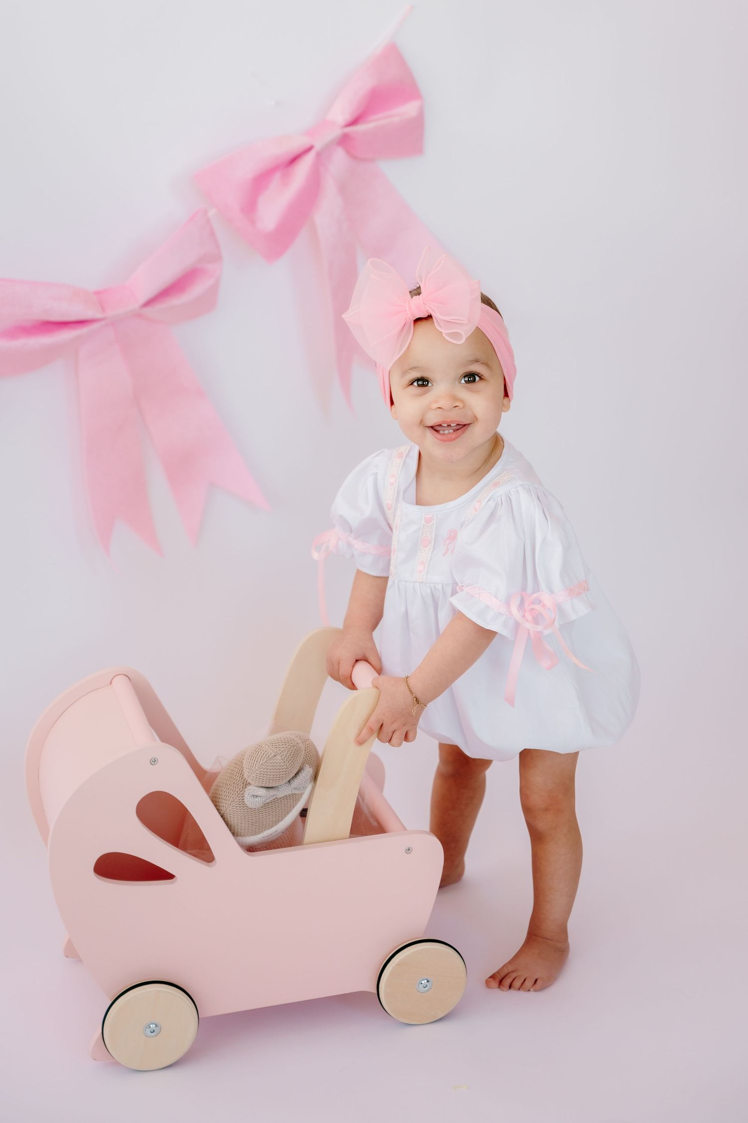 Baby playing with pink wooden toy car under pink bow garland.