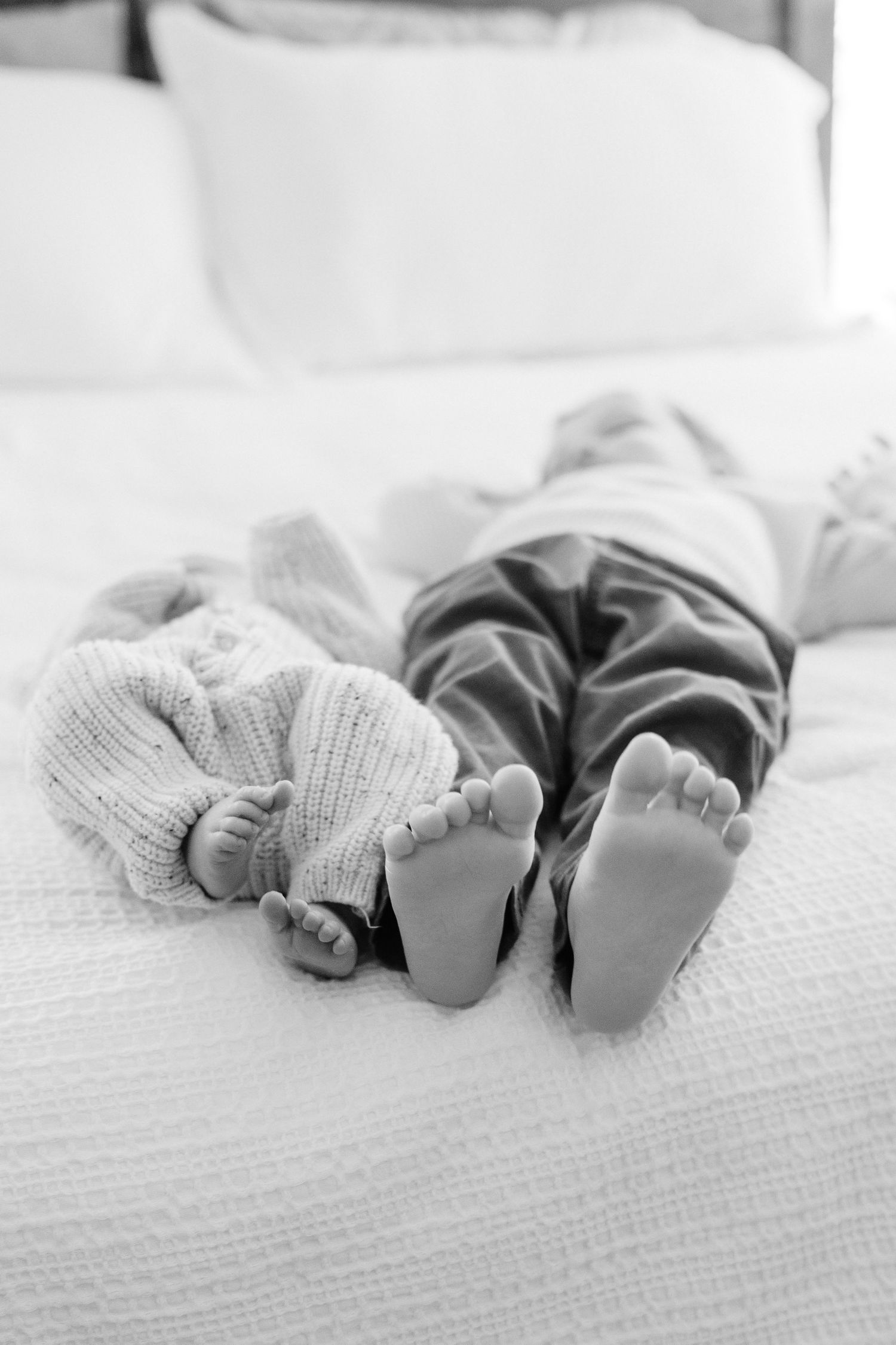 Black and white image of two pairs of feet on white bedding.