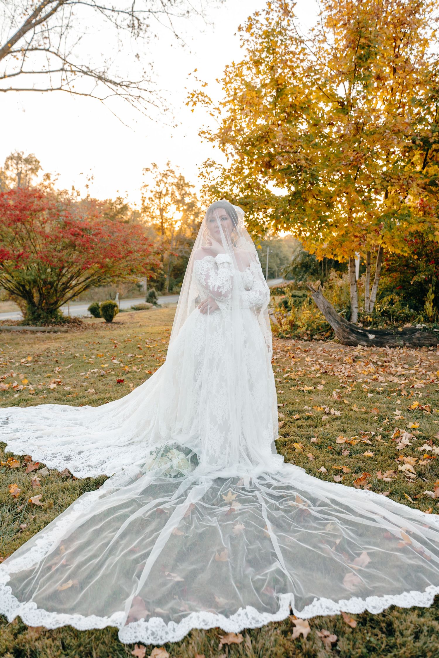 Cathedral length lace veil spread dramatically across autumn grass with fallen leaves.