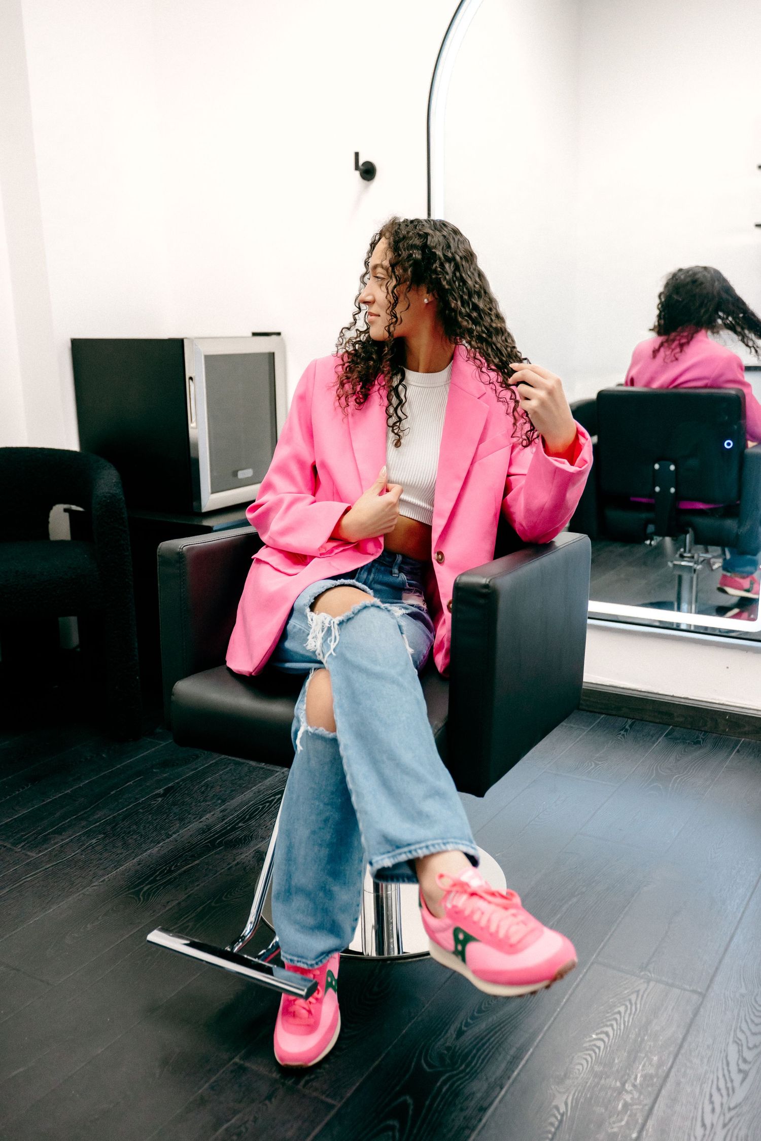 Person lounging in a pink blazer and light jeans with matching pink sneakers on a black couch.