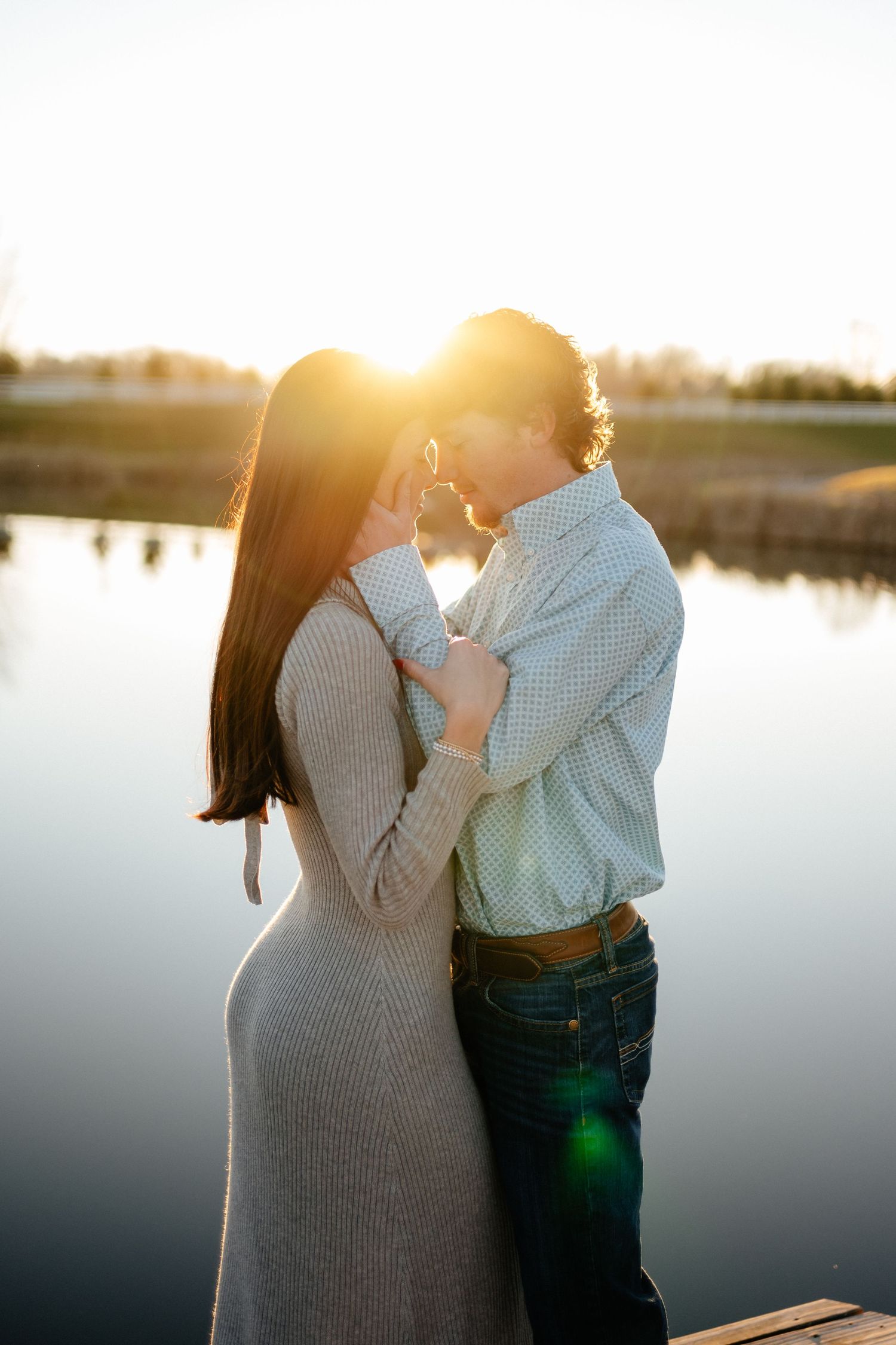 Romantic sunset engagement photos by a lake with golden hour lighting.