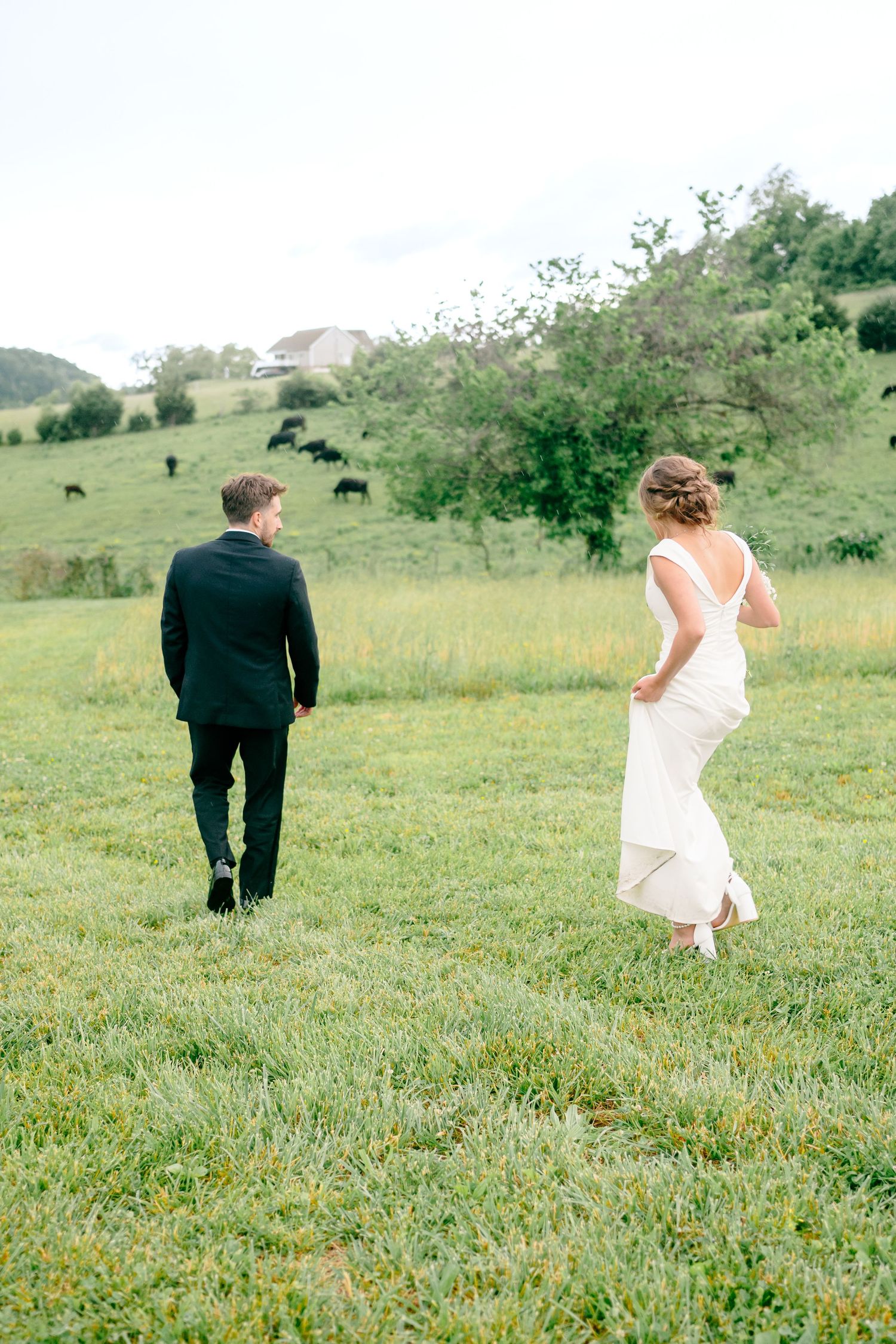 Wedding couple walks through green meadow with mountains in background.
