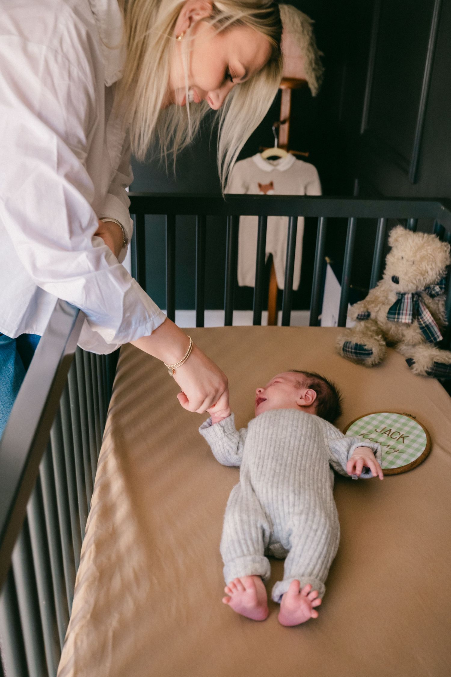 A baby lying in a crib being cared for by someone in a white shirt.