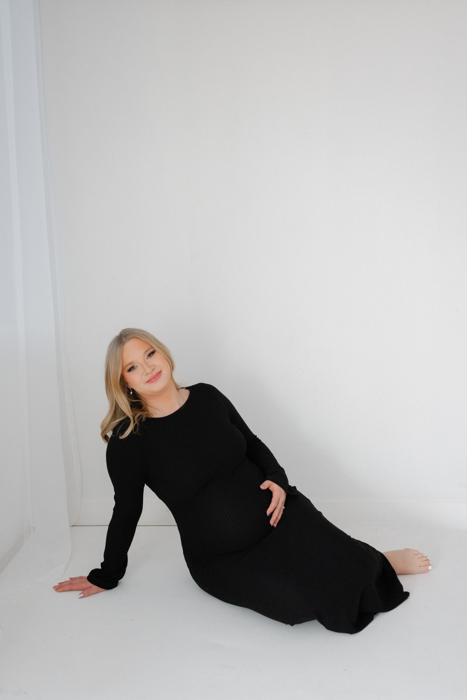 Maternity photo series showing a woman in black dress posing gracefully against a white backdrop.