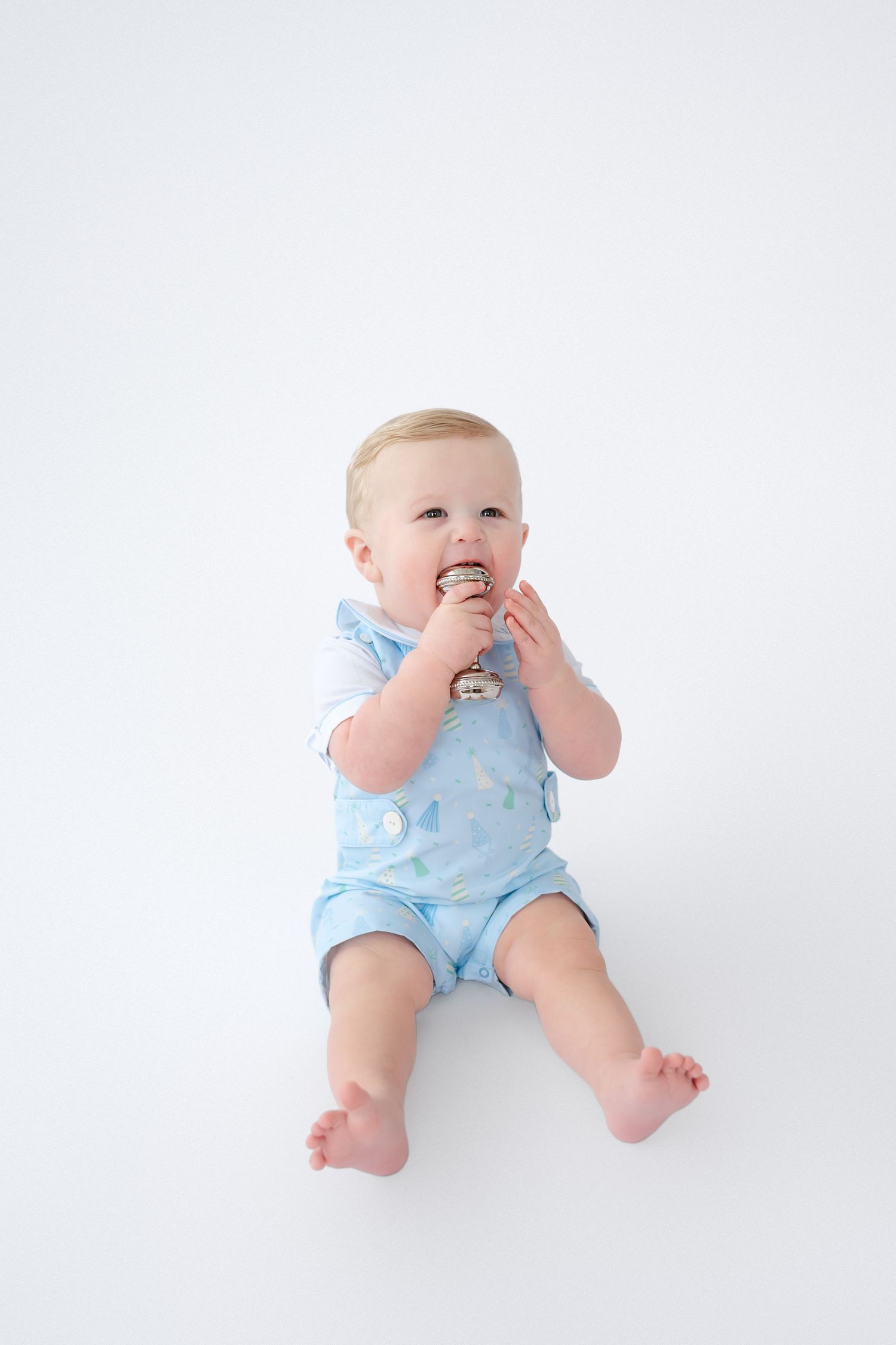 Baby wearing light blue romper lies on white backdrop in three similar poses during professional photo session.