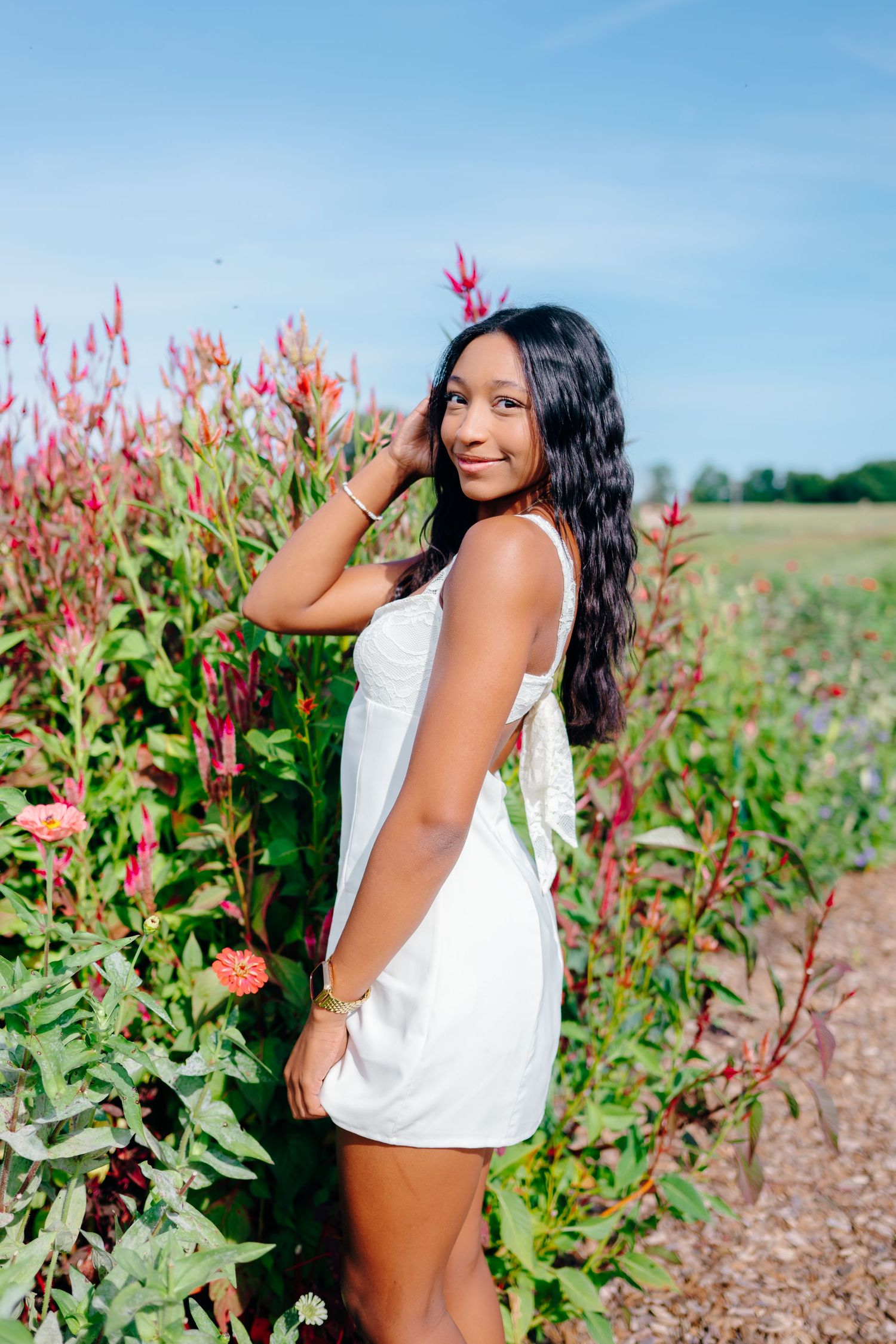 Portrait session in a field with red flowering plants and clear blue sky.
